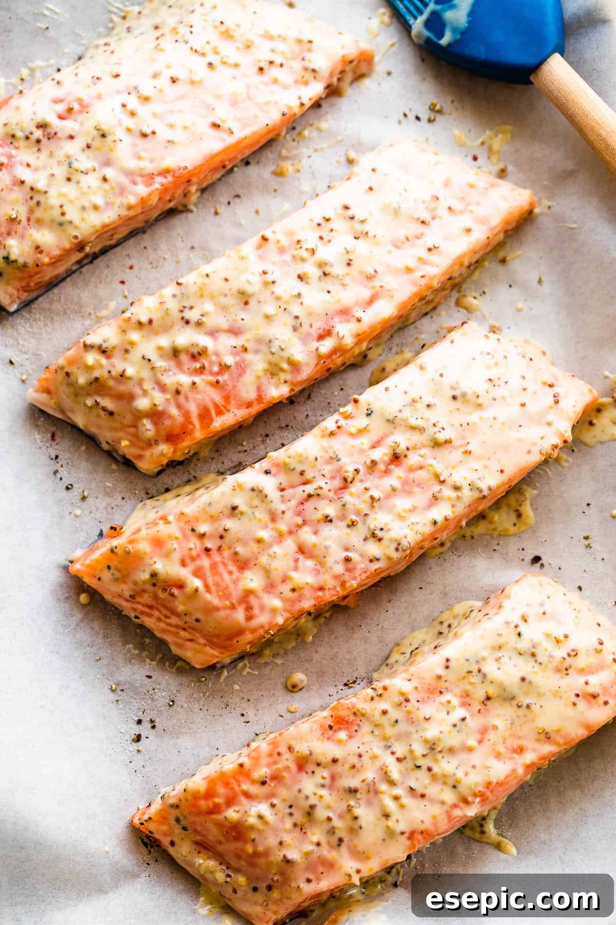 This baked Maple Mustard Salmon recipe is lightly seasoned, then brushed with a sweet and tangy sauce made from maple syrup and Dijon mustard! four raw salmon fillets arranged neatly on a baking sheet, ready for seasoning