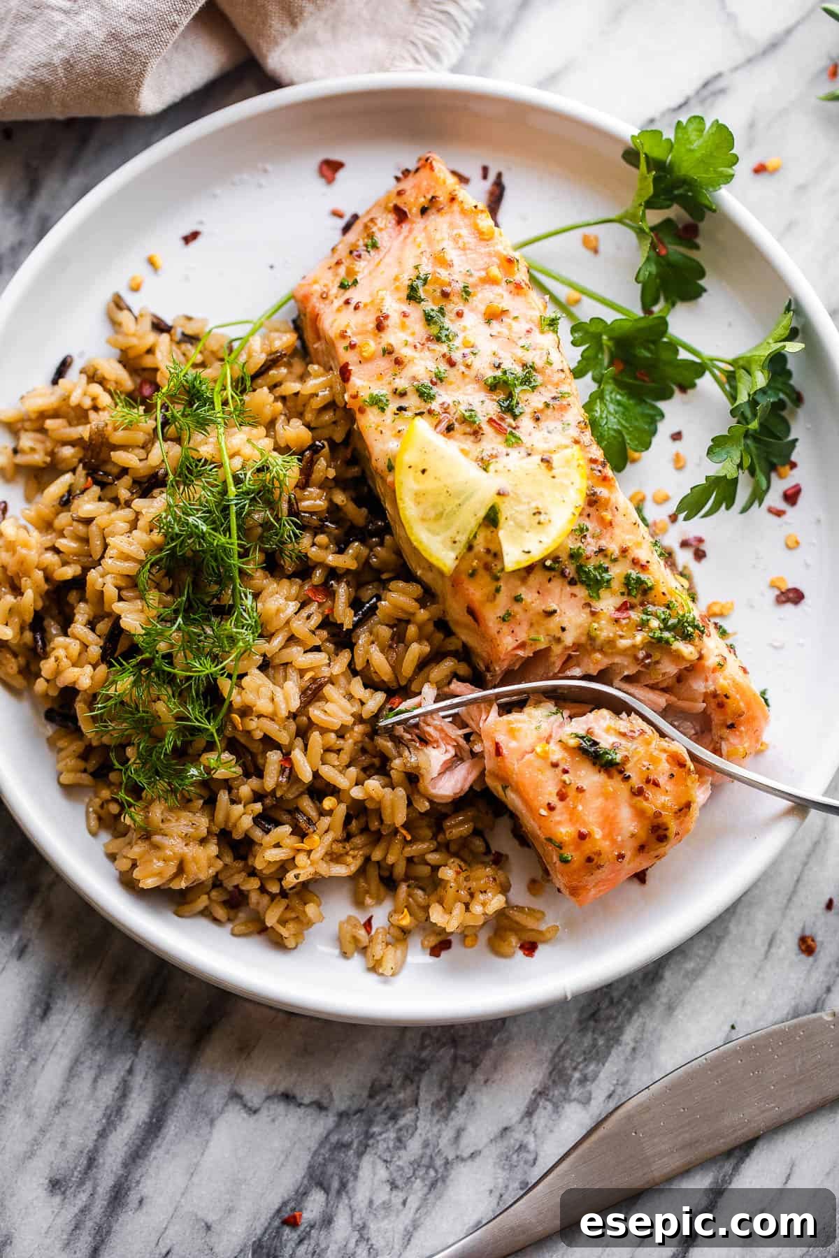 This baked Maple Mustard Salmon recipe is lightly seasoned, then brushed with a sweet and tangy sauce made from maple syrup and Dijon mustard! salmon fillet on white plate served with wild brown rice and fresh herbs