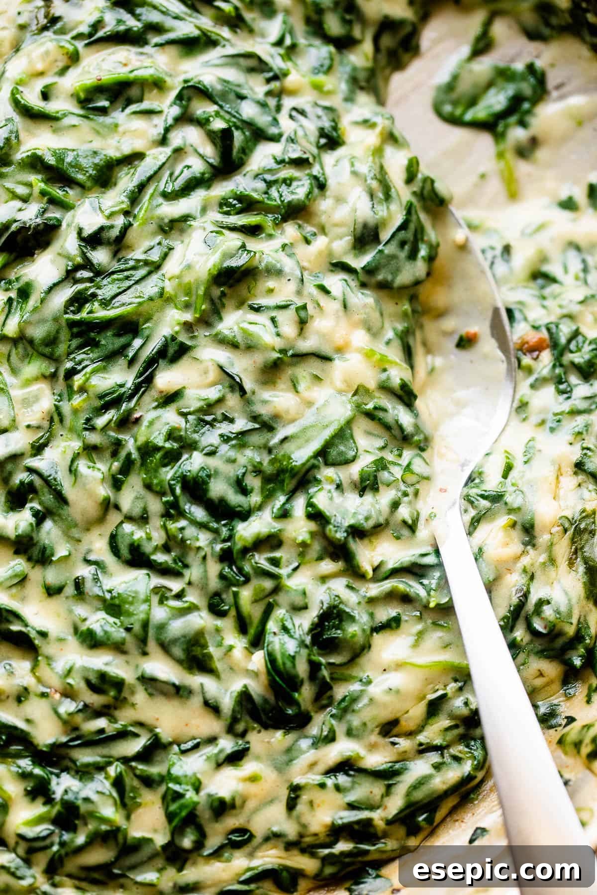 A large serving spoon stirring creamy, vibrant green steakhouse creamed spinach in a skillet, highlighting its rich texture.