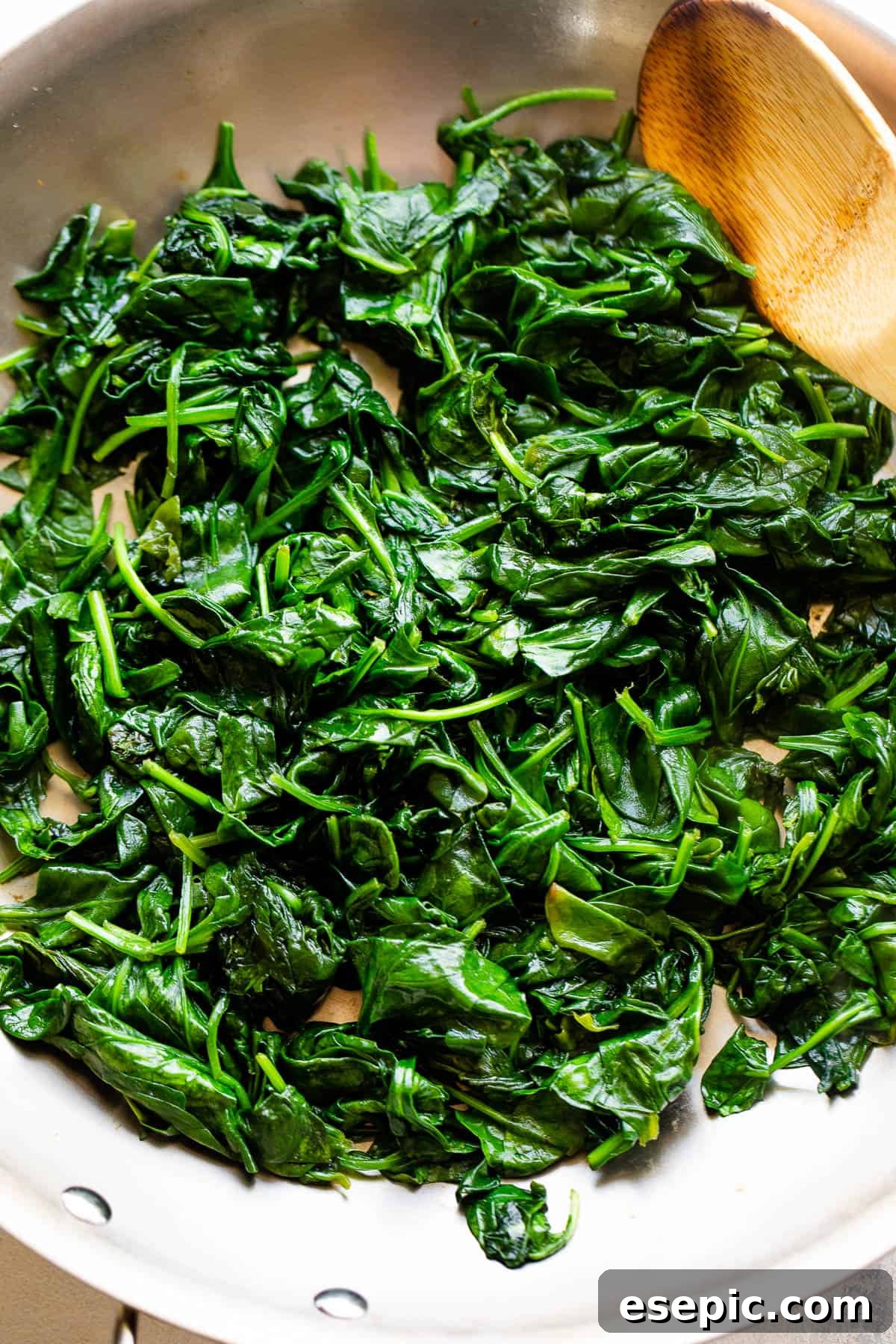 Fresh baby spinach wilting in a large stainless steel skillet, preparing for the creamy sauce.