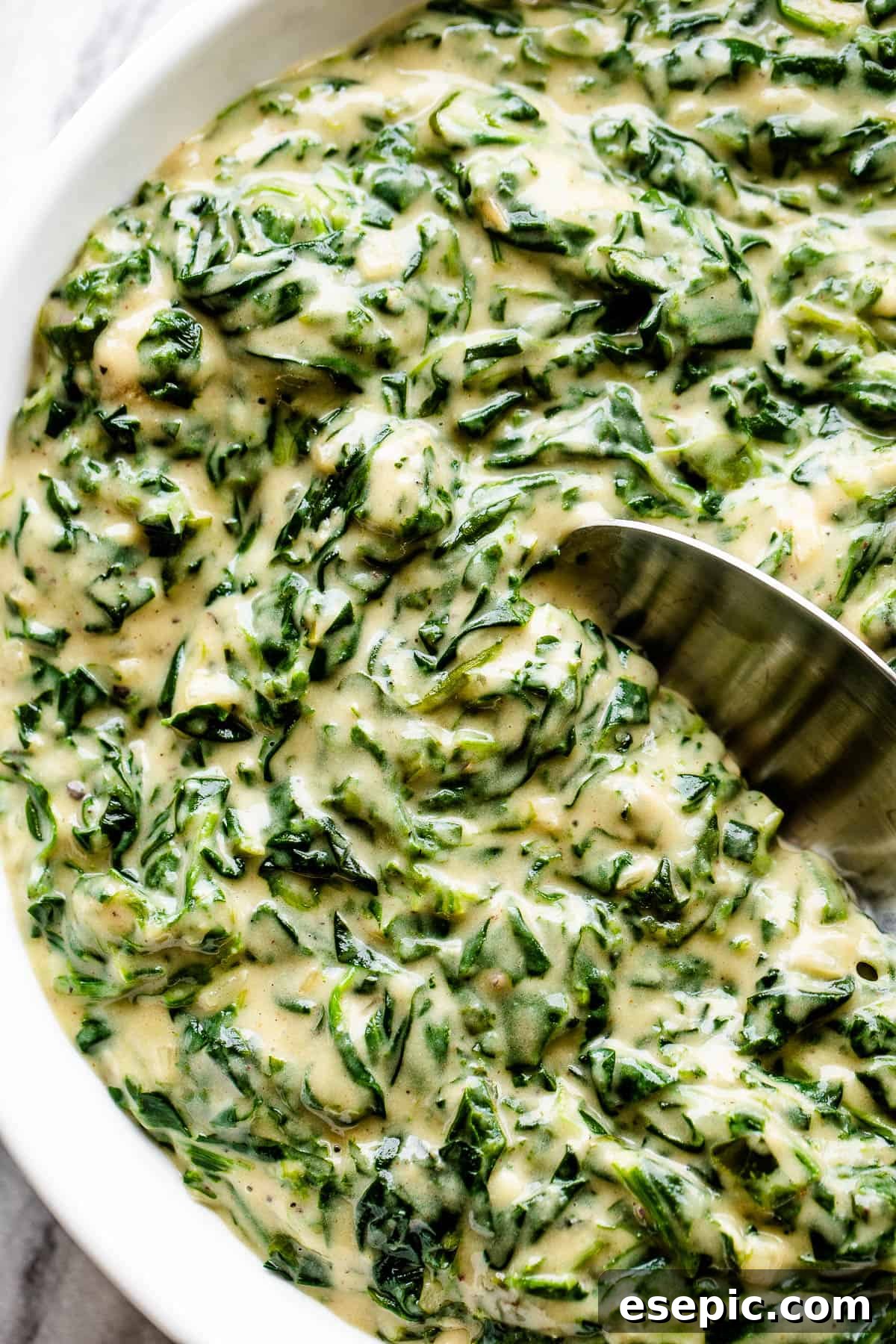 A white bowl filled with creamy steakhouse creamed spinach, with a spoon inside, ready to be enjoyed as a classic side dish.