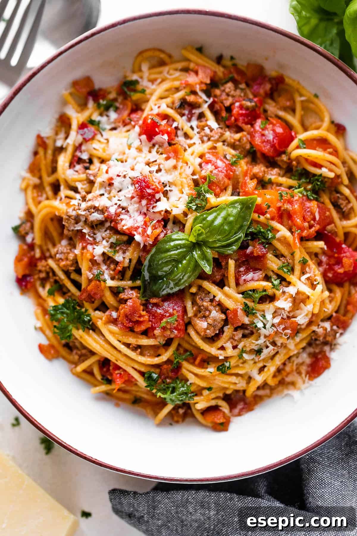 Overhead shot of a bowl of Instant Pot spaghetti topped with fresh tomatoes and basil leaves, ready to serve.