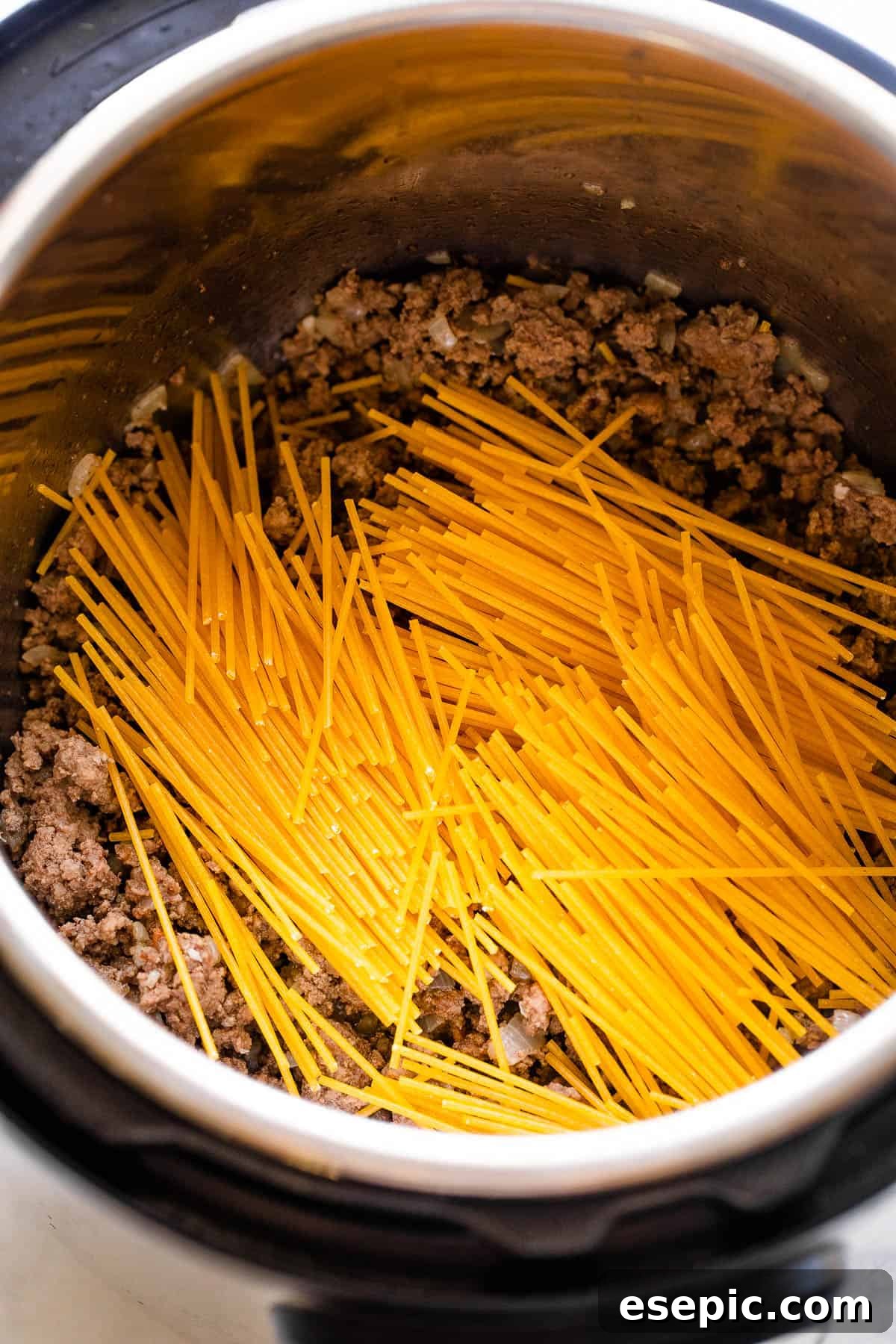 Dry spaghetti noodles being broken over ground beef and onions in the Instant Pot liner.