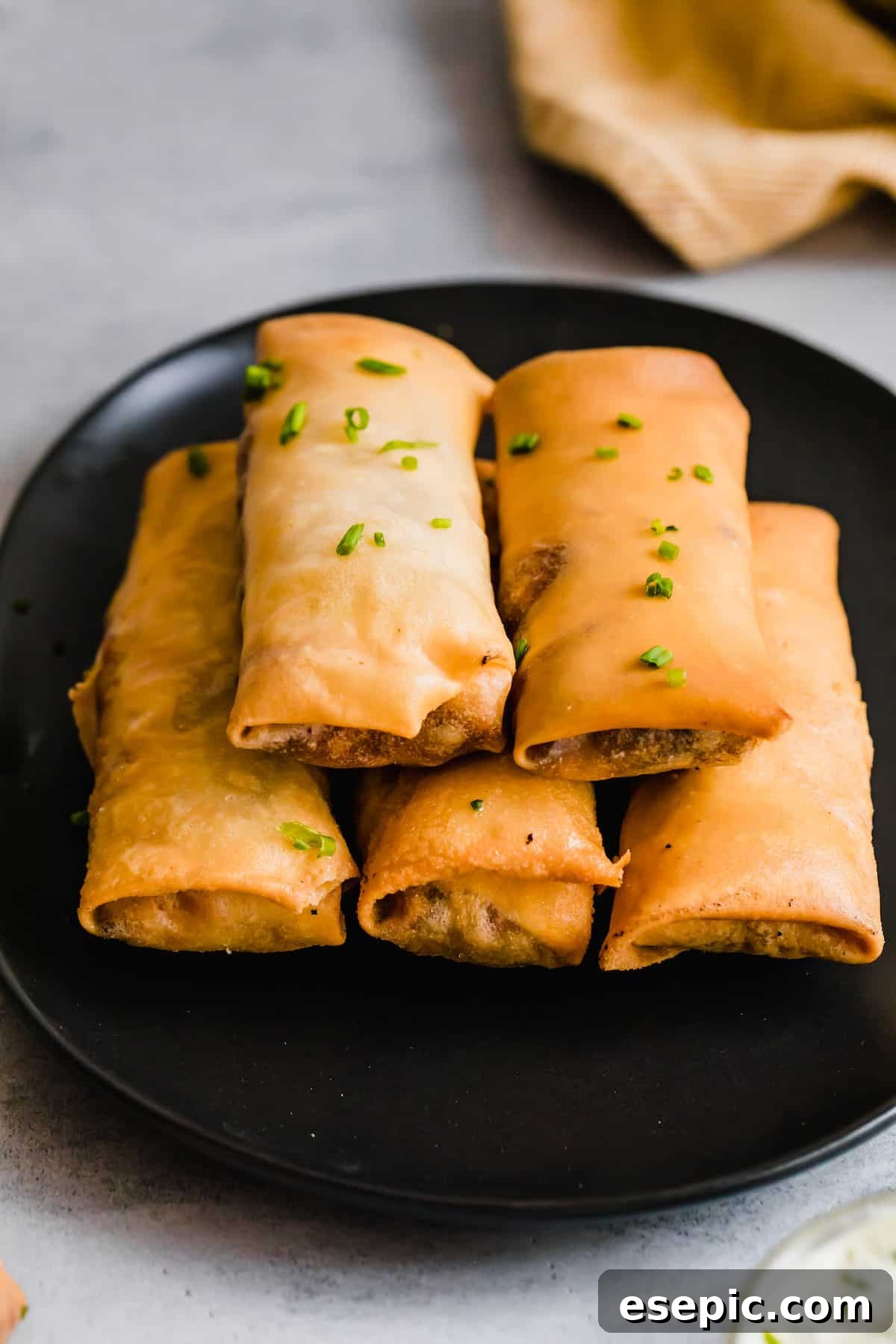 Five Egg Rolls Piled Neatly on a Shiny Black Plate