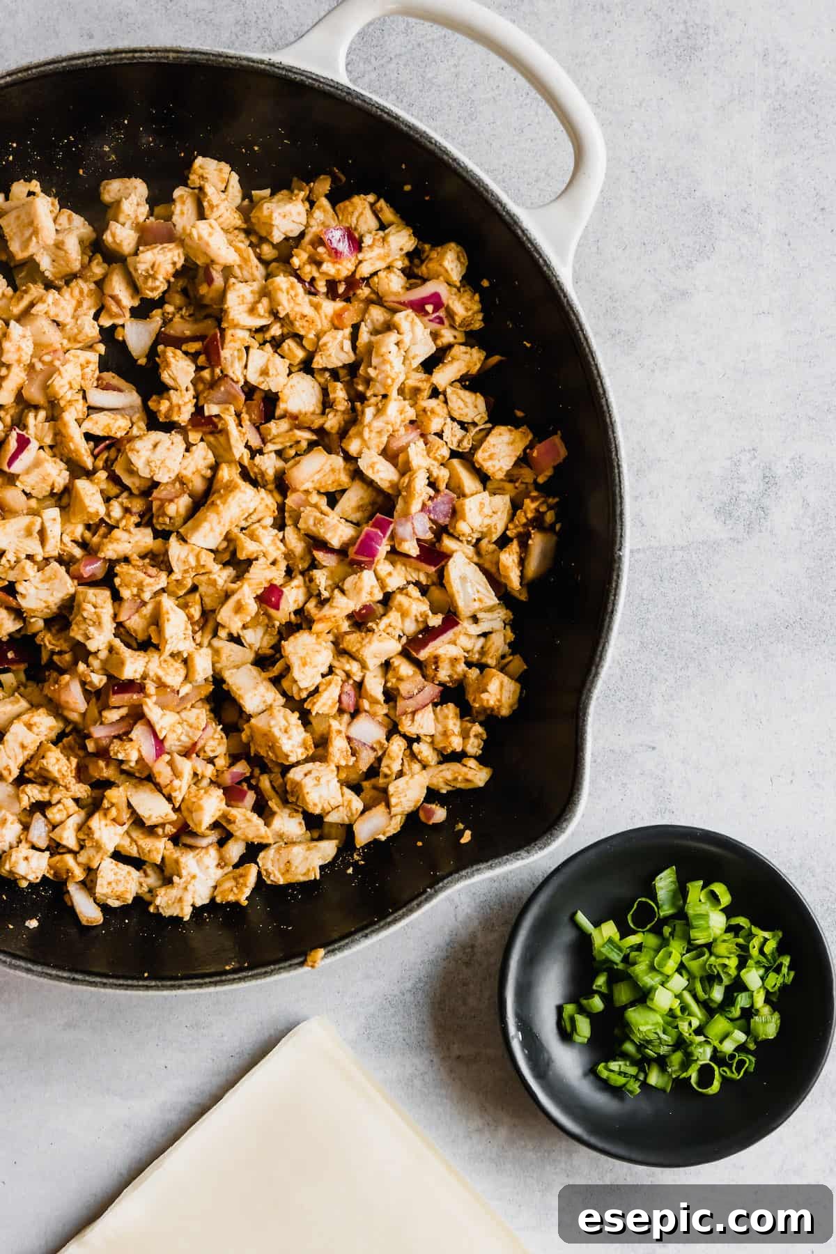 Spices, Diced Chicken and Onions in a Pan Next to a Dish of Chopped Scallions