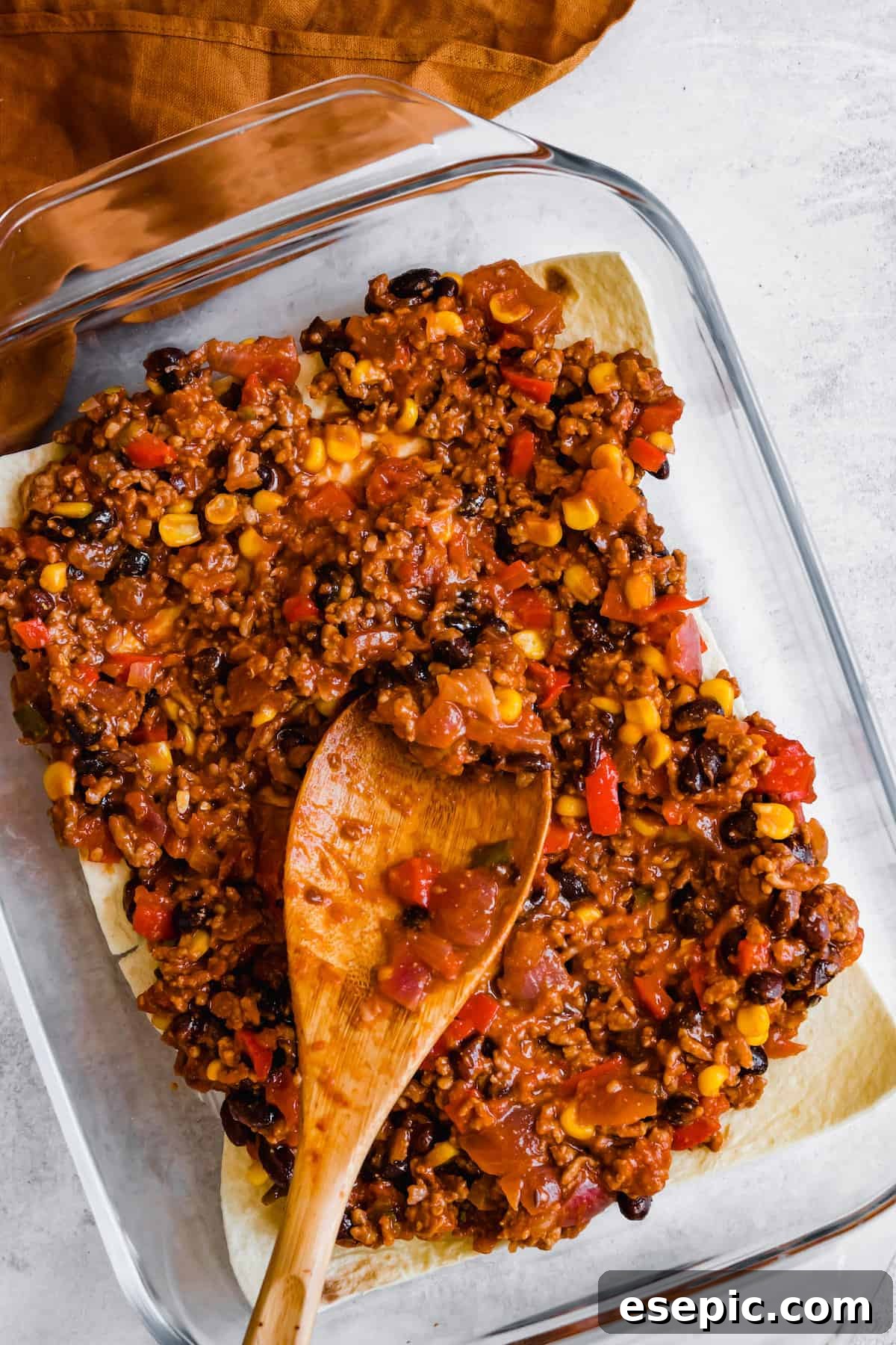 A Wooden Spoon Spreading a Layer of Lasagna Filling Over a Layer of Tortillas