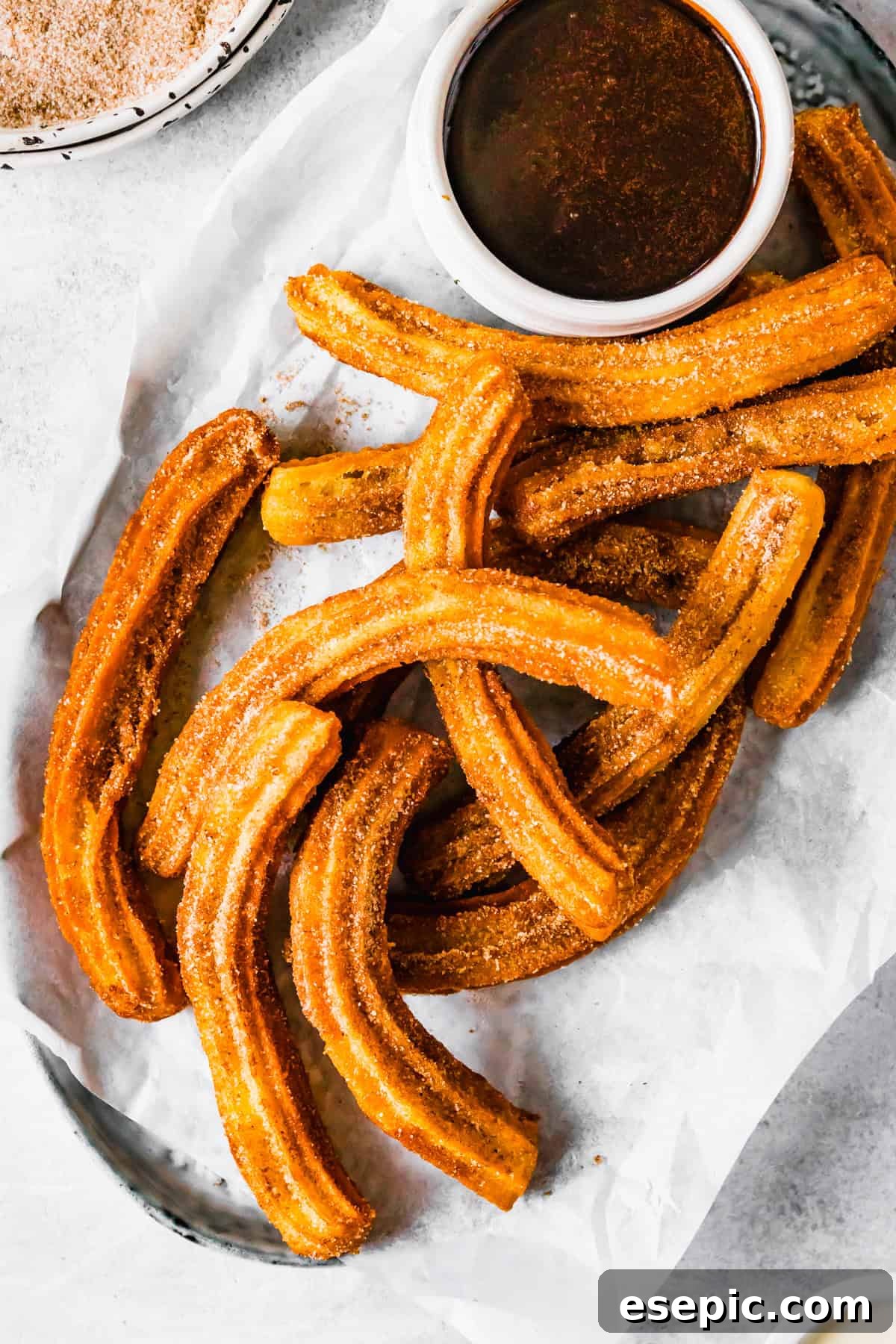Crispy, golden homemade churros elegantly arranged on a plate, accompanied by a small bowl of luxurious dark chocolate dipping sauce. A perfect dessert or snack.