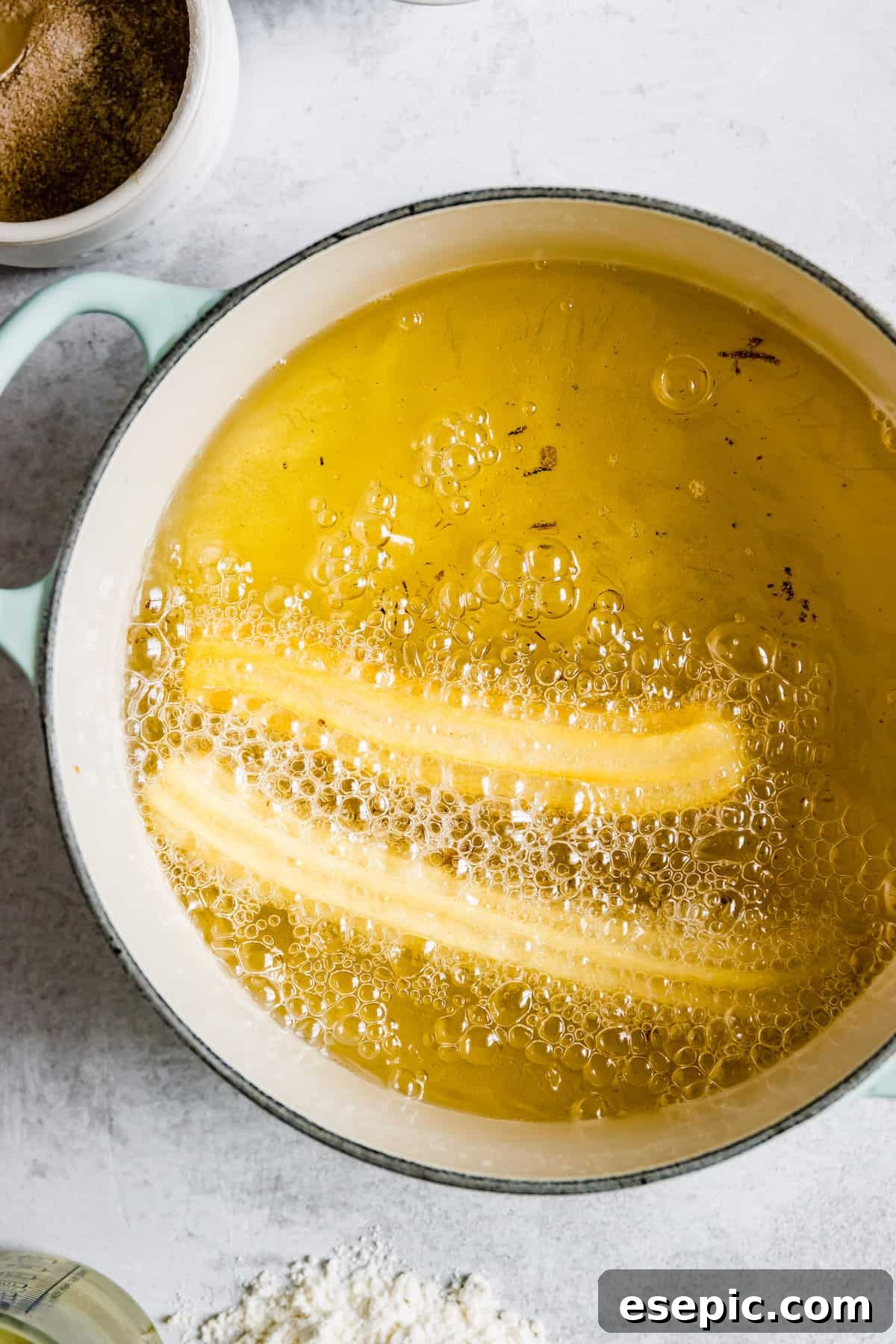 Two golden-brown churros actively frying in a pot of hot oil, illustrating the cooking process.