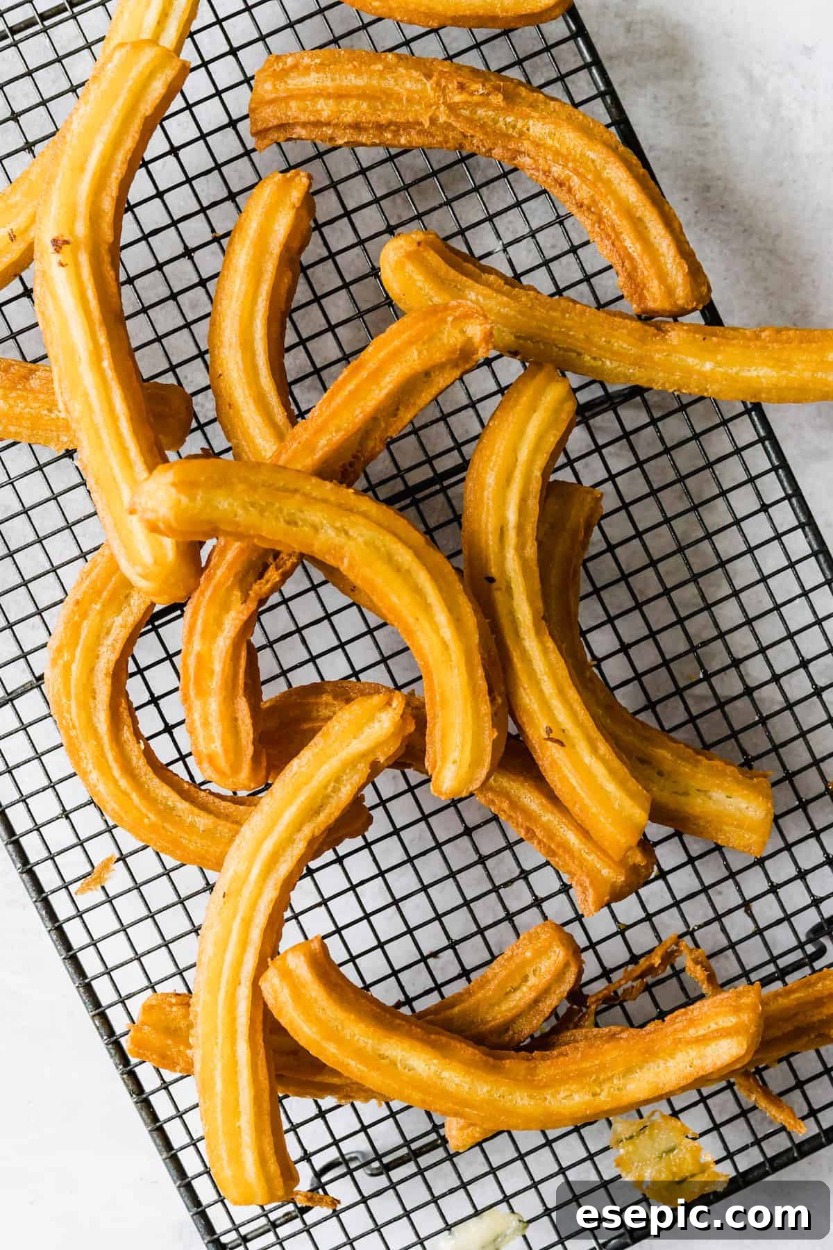 A cooling rack laden with numerous freshly fried, golden churros, ready for their cinnamon sugar coating.