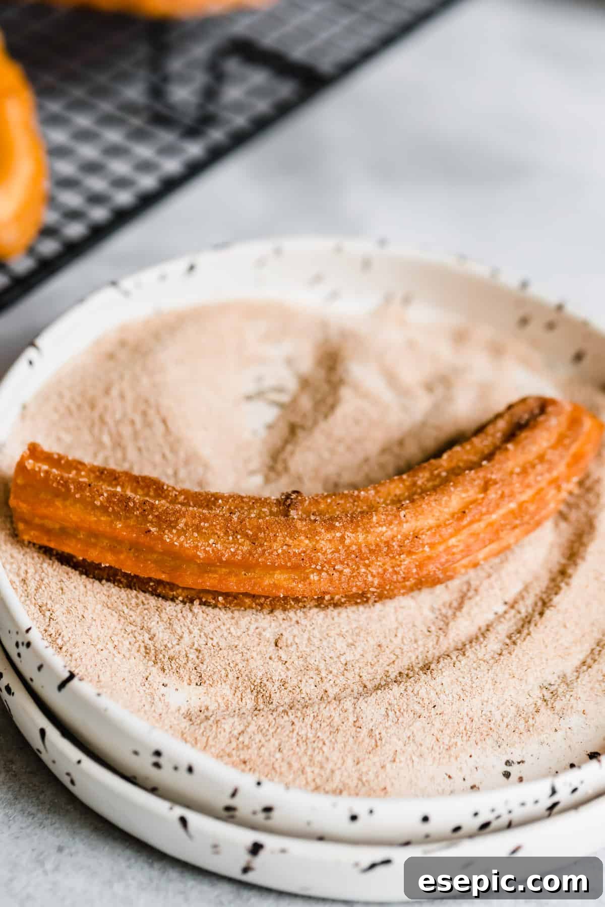A single churro being generously rolled in a shallow bowl filled with cinnamon sugar, ensuring full coverage for that perfect sweet finish.
