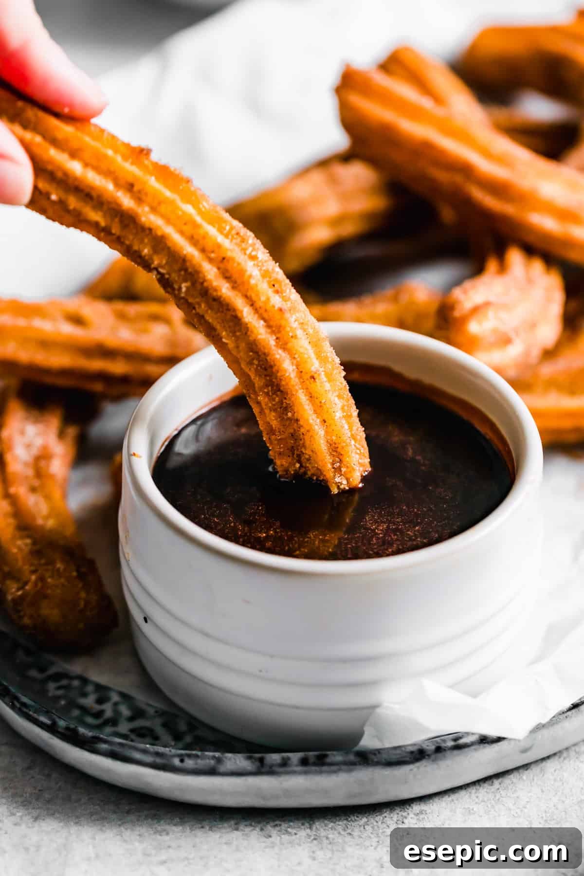 A hand dipping a crispy homemade churro into a bowl of rich, velvety chocolate sauce, highlighting the perfect pairing.