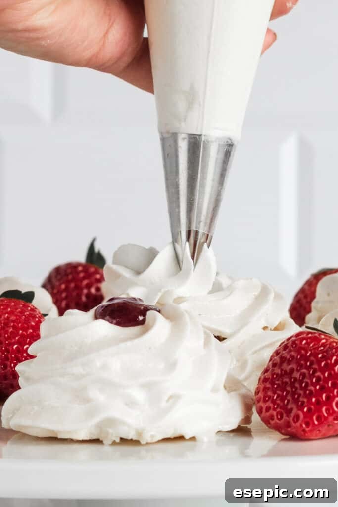 Effortless Strawberry Meringue Nests 11 A hand expertly piping fluffy whipped cream onto a dessert, showcasing the perfect texture for pavlova topping.