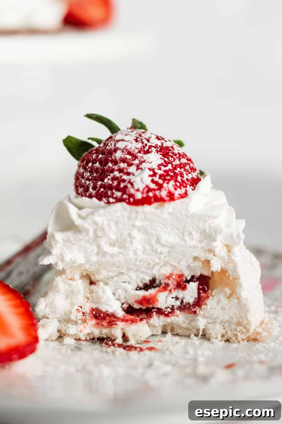 Effortless Strawberry Meringue Nests 13 A close-up view of a mini pavlova nest cut open, revealing the vibrant strawberry jam filling beneath the creamy whipped topping.