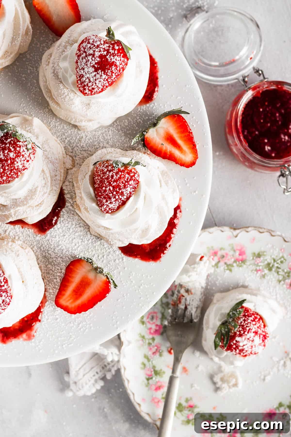 Effortless Strawberry Meringue Nests 3 Overhead shot of several mini pavlovas, each beautifully topped with whipped cream, fresh strawberries, and a dusting of powdered sugar.