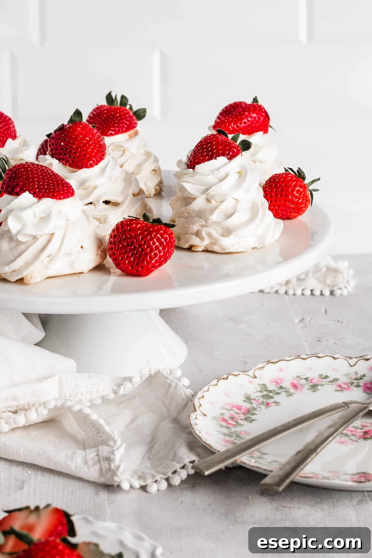 Effortless Strawberry Meringue Nests 5 A beautiful presentation of mini pavlovas on a cake stand, generously topped with whipped cream and fresh strawberries.