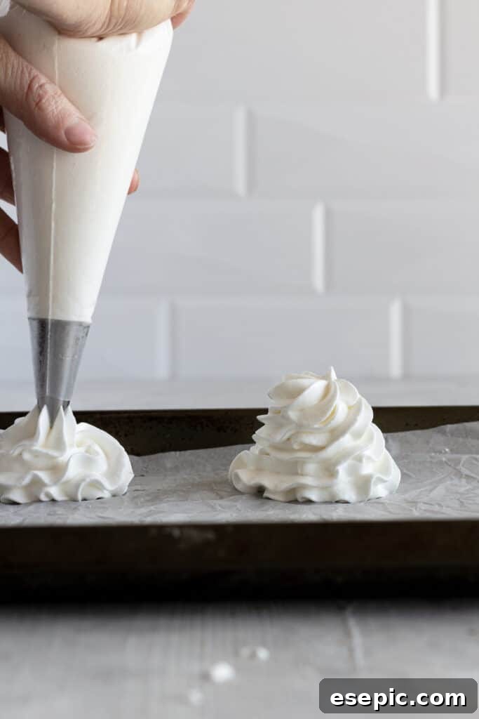 Effortless Strawberry Meringue Nests 8 A piping bag carefully shaping pavlova nests onto a parchment-lined baking sheet, creating small indentations for filling.