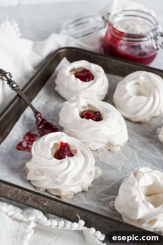 Effortless Strawberry Meringue Nests 10 A pavlova nest being carefully filled with a spoonful of glistening strawberry jam, ready for the next layer of topping.