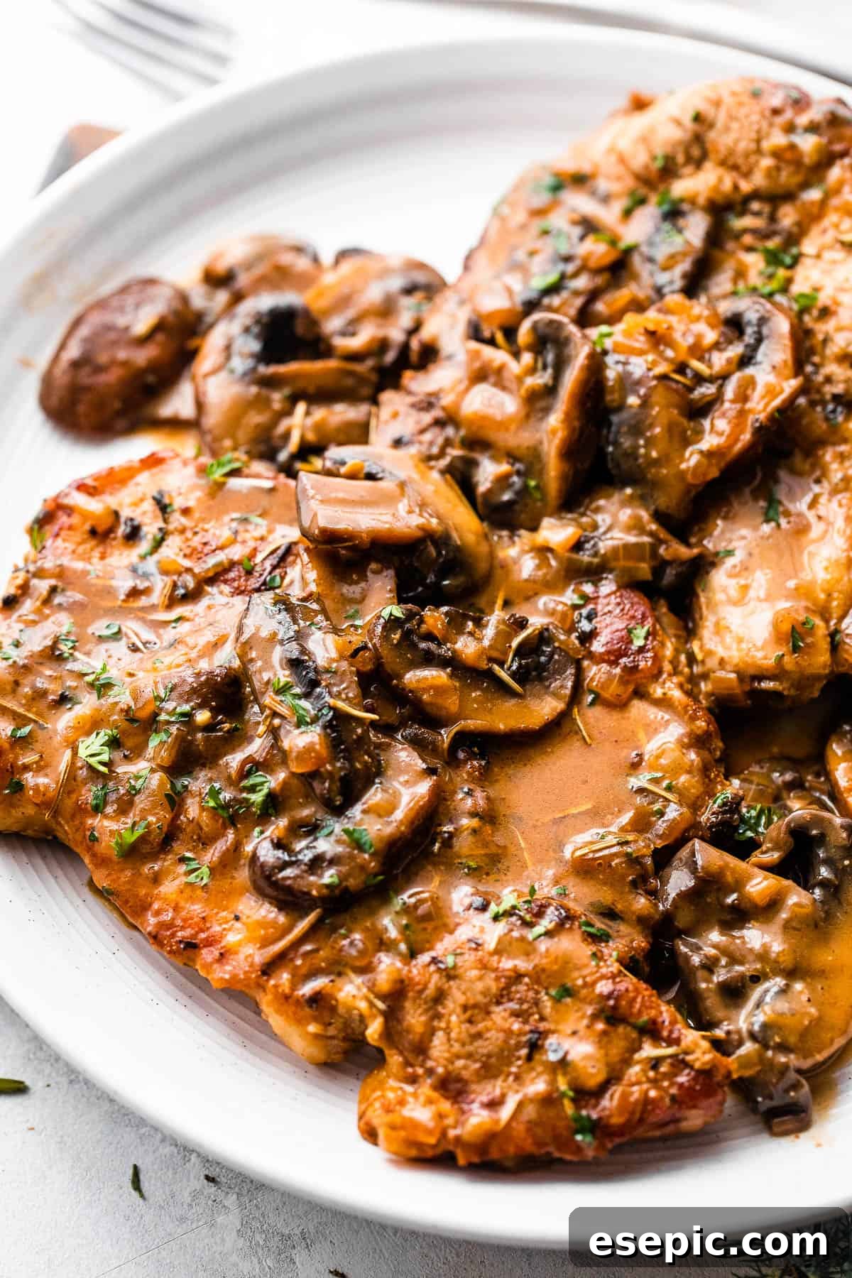 Two bone-in pork chops served elegantly on a white plate, generously coated with creamy mushroom gravy