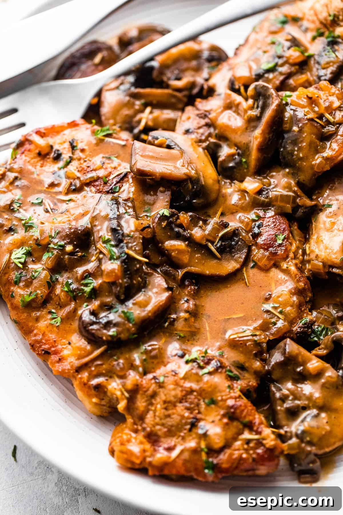 Two bone-in pork chops served on a white plate, topped with generous portions of creamy mushroom gravy