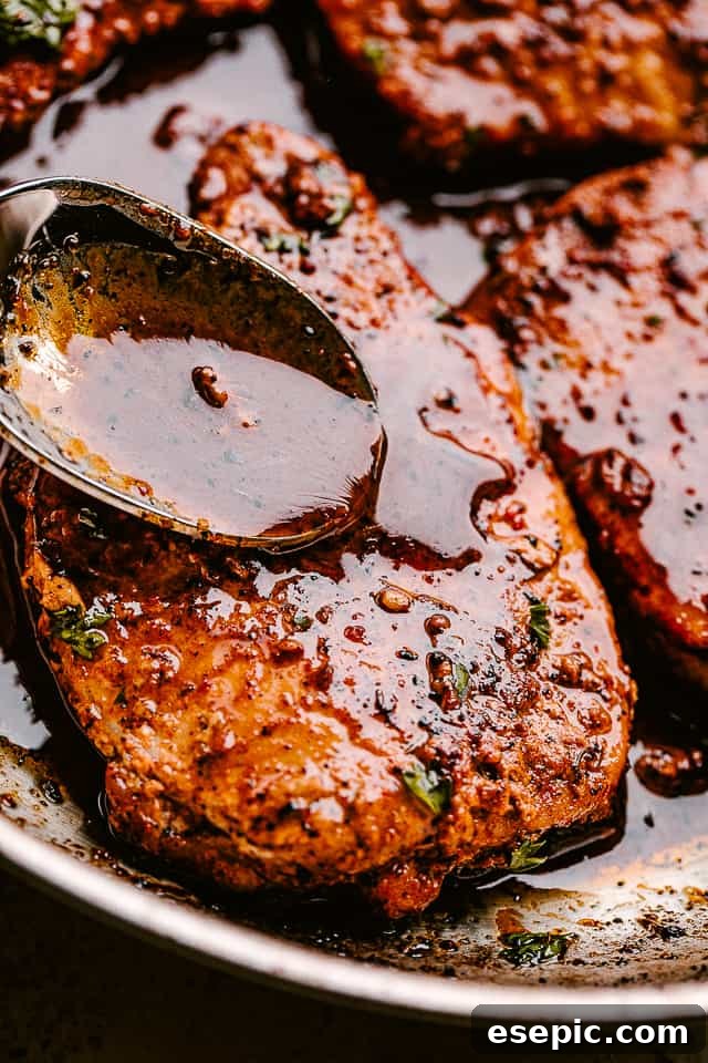 Hand spooning rich honey garlic sauce over pan-fried pork chops in a skillet