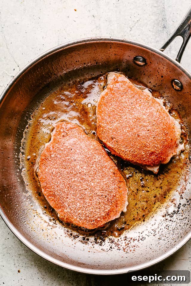 Close-up of boneless pork chops seasoned with garlic parmesan rub in a skillet