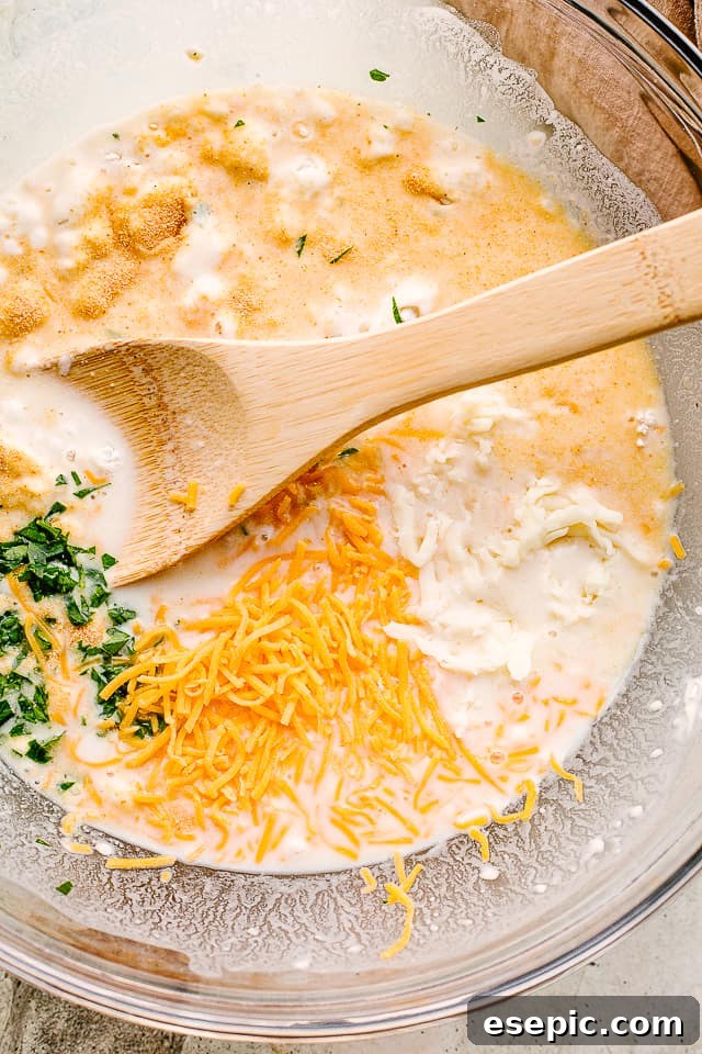 Making warm and crusty homemade bread is easier than you’ve imagined with this no knead cheese bread recipe. Cheesy, crusty, and oh-so-good! Close-up of dough ingredients being mixed in a large bowl with a wooden spoon.