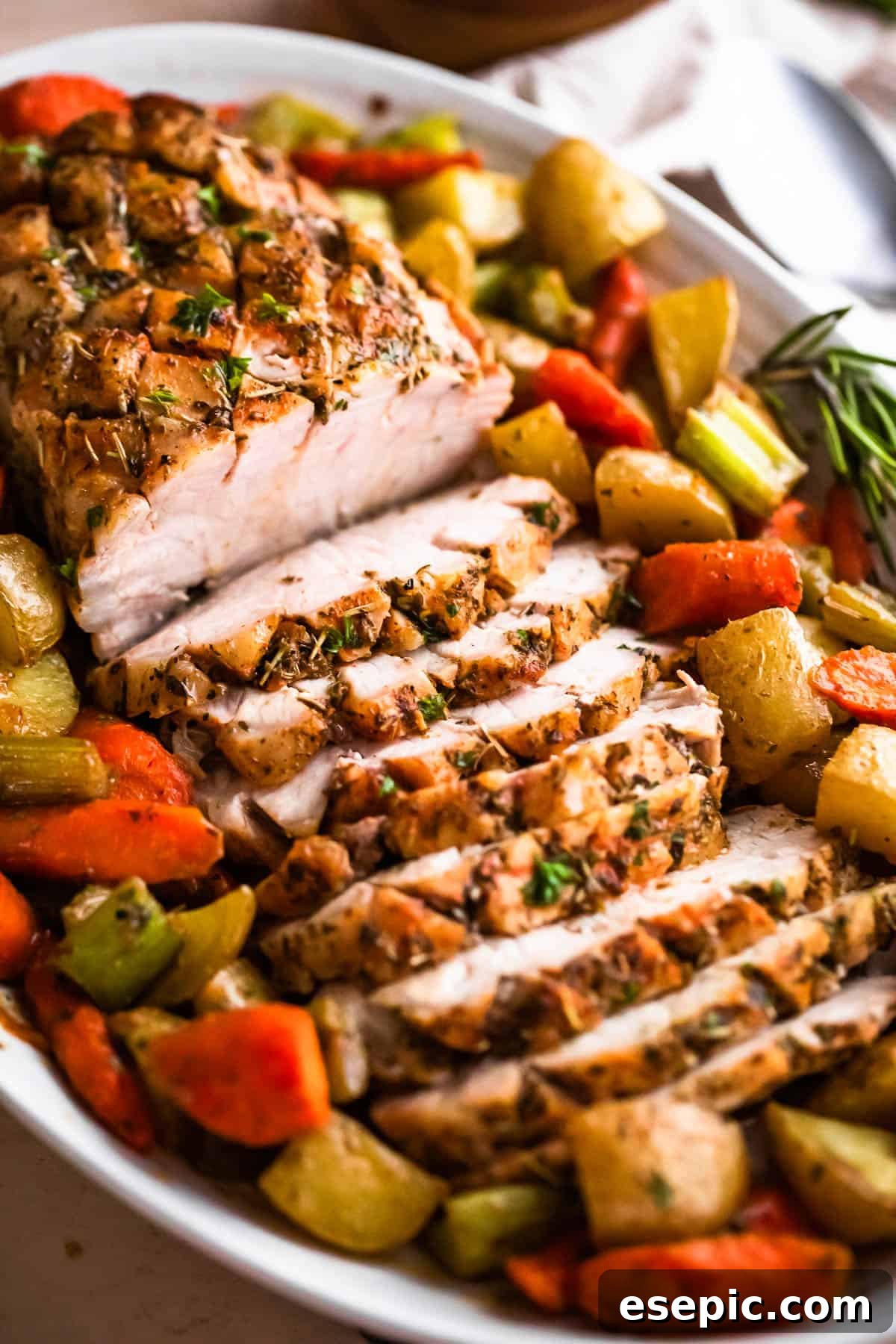 Garlic Herb Pork Loin with Roasted Root Vegetables 2 Side shot of an oval plate with cooked and sliced pork loin roast and roasted vegetables arranged around the roast, ready to serve.