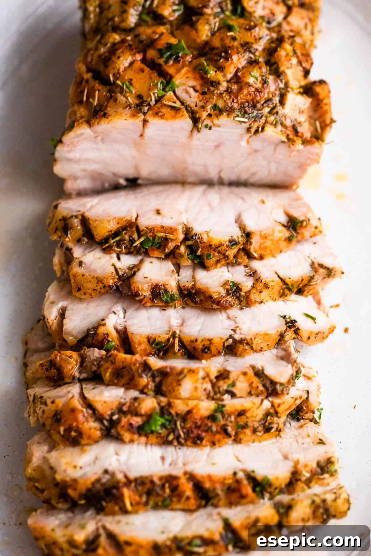 Garlic Herb Pork Loin with Roasted Root Vegetables 6 Overhead shot of a cooked and sliced pork roast, beautifully presented on a white background, highlighting its golden crust and tender interior.