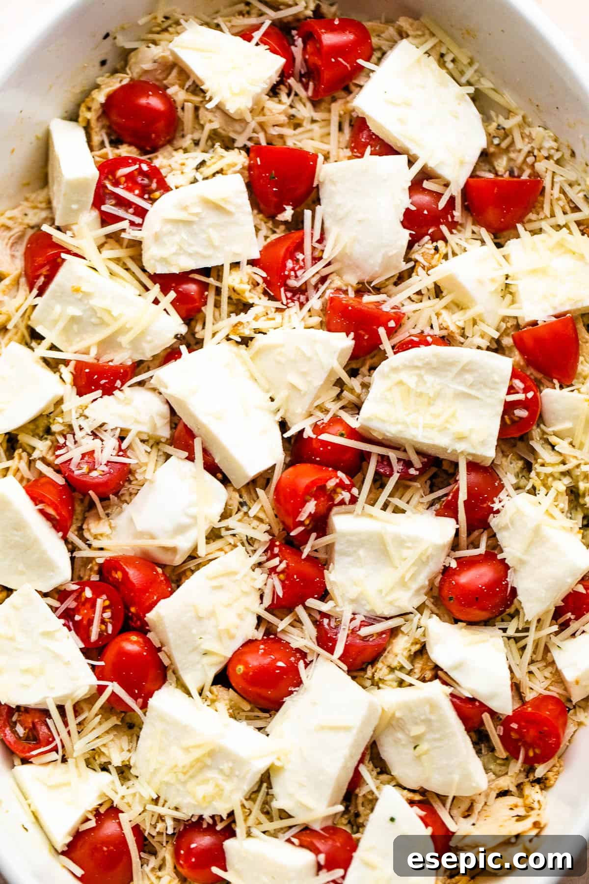 A white baking dish filled with Caprese Chicken Casserole, topped with large chunks of fresh mozzarella and bright red cherry tomatoes, ready for baking.