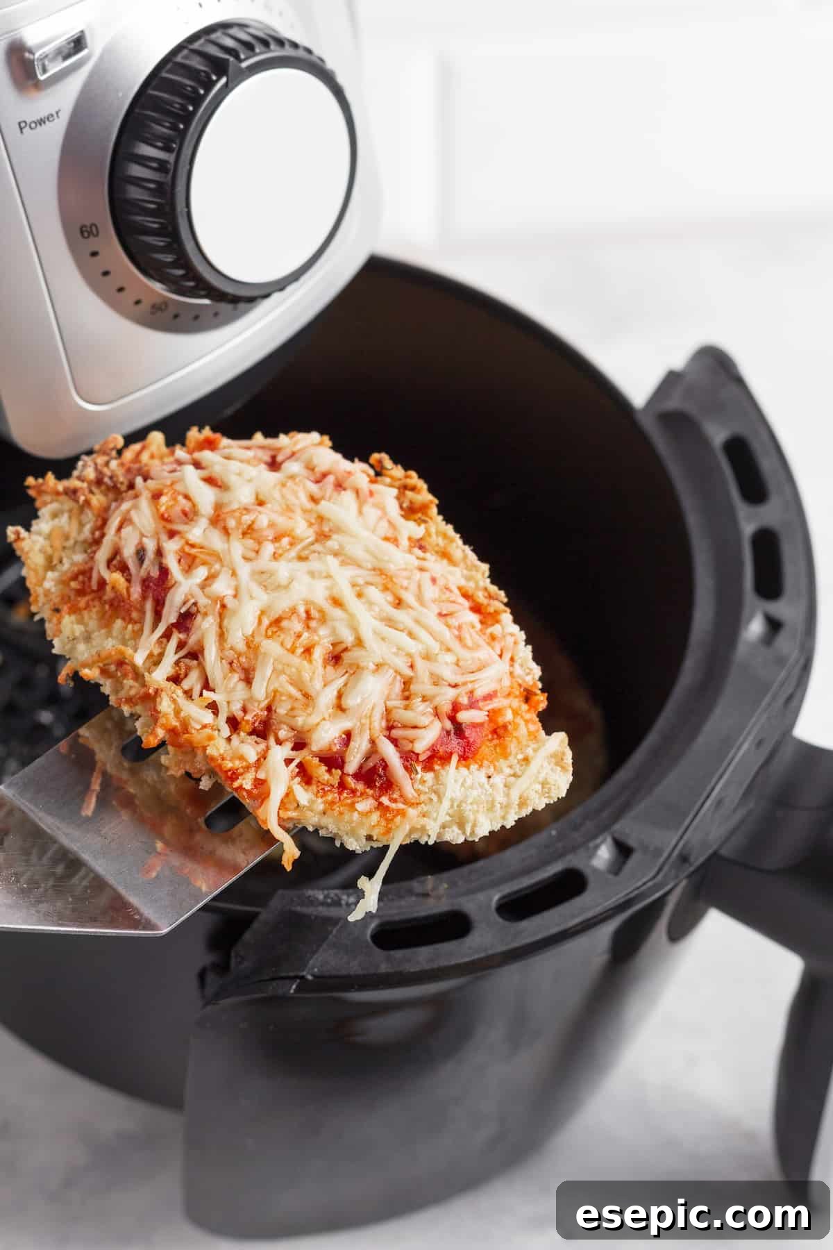 Crispy Air Fryer Chicken Parm 4 A breaded chicken cutlet being carefully lifted from an air fryer basket with a metal spatula, ready to be topped with sauce and cheese.