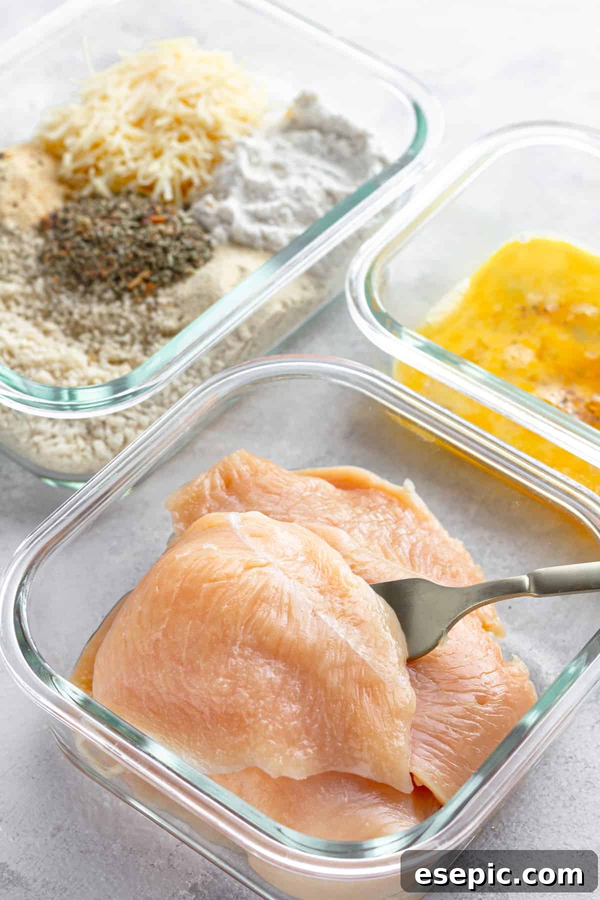 Crispy Air Fryer Chicken Parm 5 Three glass bowls displaying the breading station: raw chicken, a whisked egg mixture, and a seasoned panko breadcrumb blend.