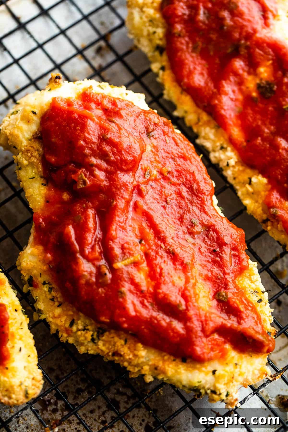Crispy Air Fryer Chicken Parm 7 Two partially cooked, breaded chicken cutlets in an air fryer basket, now topped with rich marinara sauce, ready for the final cheese layer.