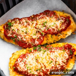 Two Pieces of Breaded, Partially Cooked Chicken Being Topped with Marinara and Shredded Parmesan Cheese