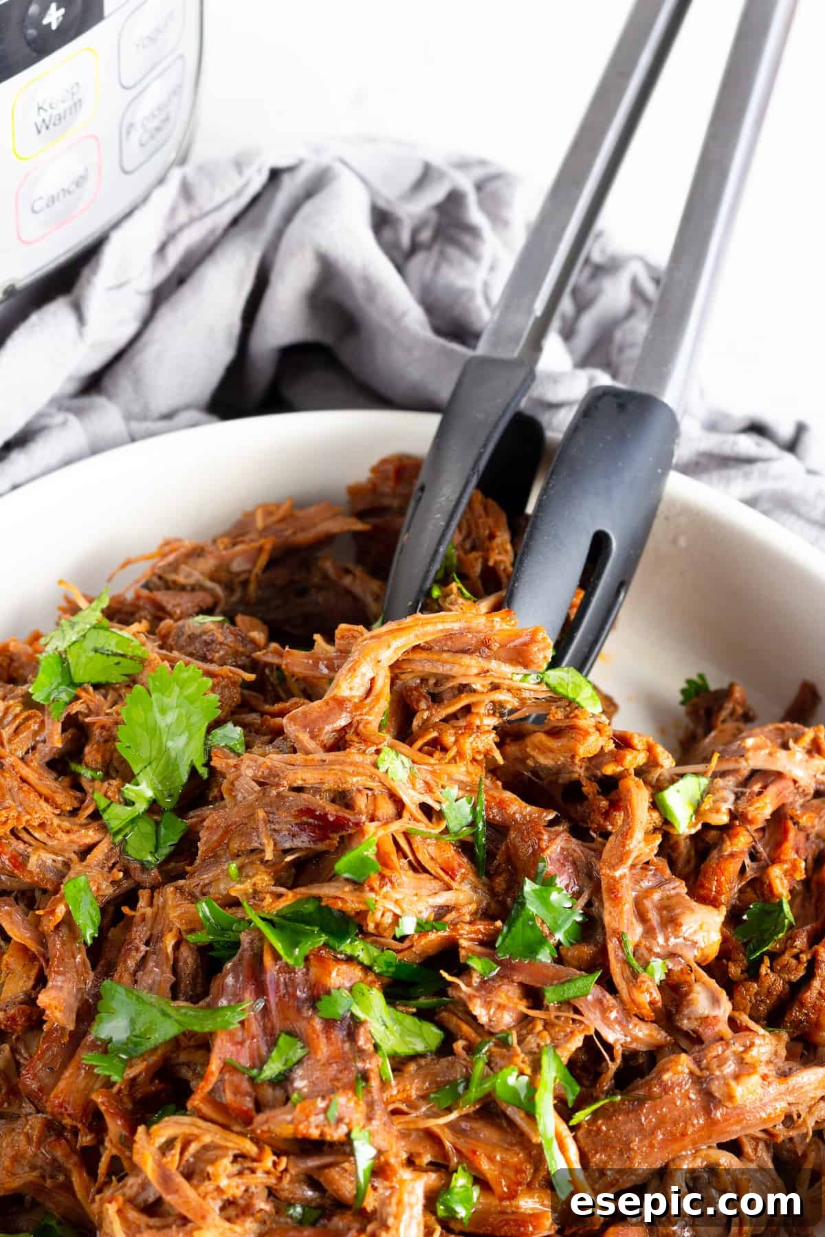 A Pair of Metal Tongs Digging Into a Bowl of Instant Pot Beef