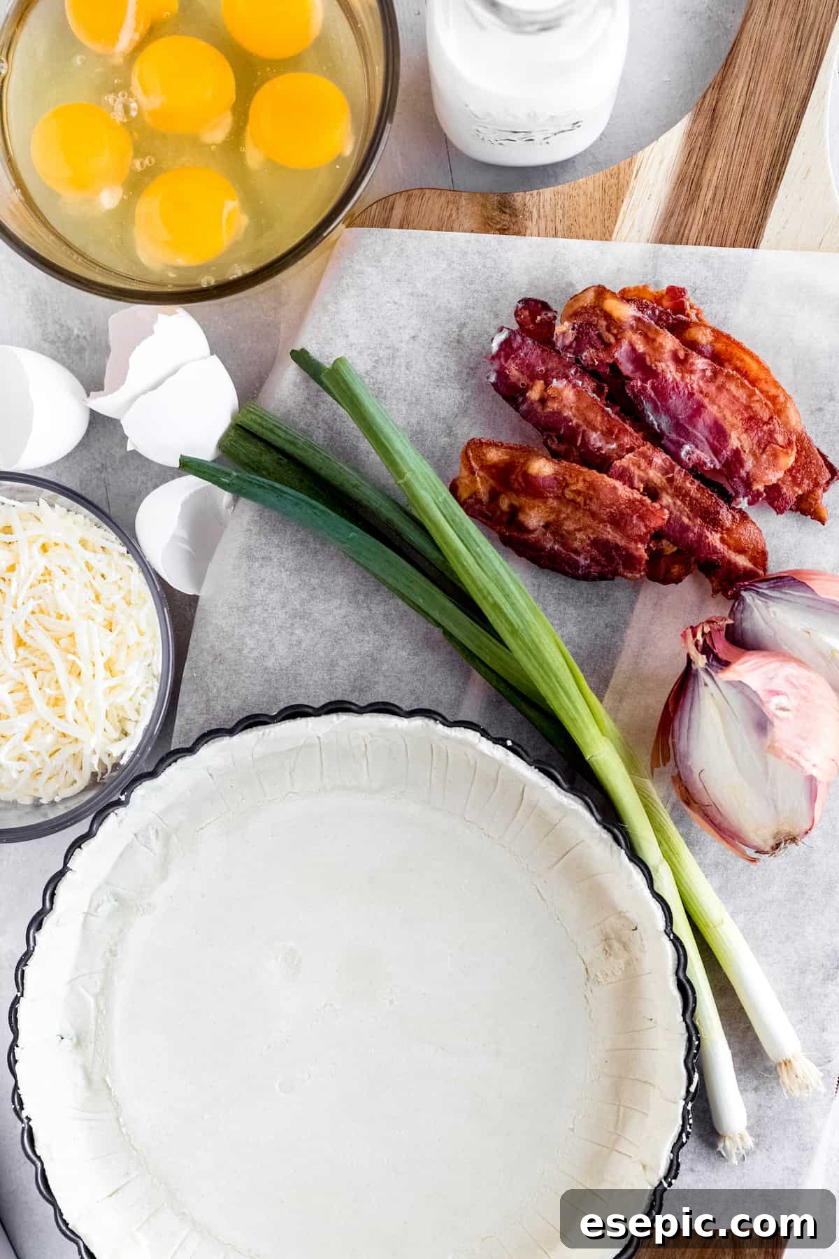 Effortlessly Delicious Bacon Quiche Lorraine 4 A curated display of all necessary quiche ingredients: a refrigerated pie crust, cooked bacon, fresh eggs, shredded Swiss cheese, and other aromatic components, ready for assembly.