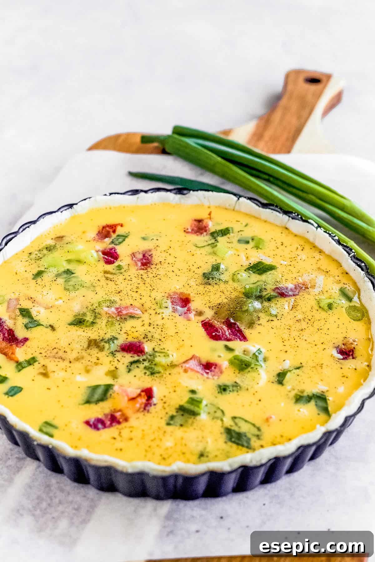 Effortlessly Delicious Bacon Quiche Lorraine 6 An unbaked Quiche Lorraine, beautifully assembled, resting on a cutting board lined with parchment paper, poised for the oven.