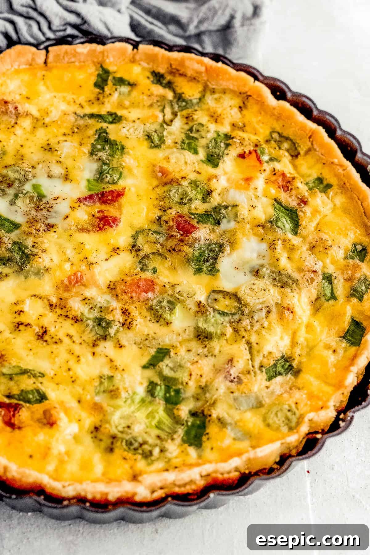 Effortlessly Delicious Bacon Quiche Lorraine 7 A freshly baked Quiche Lorraine, still warm and golden, nestled inside a sleek black quiche pan, ready to be served.