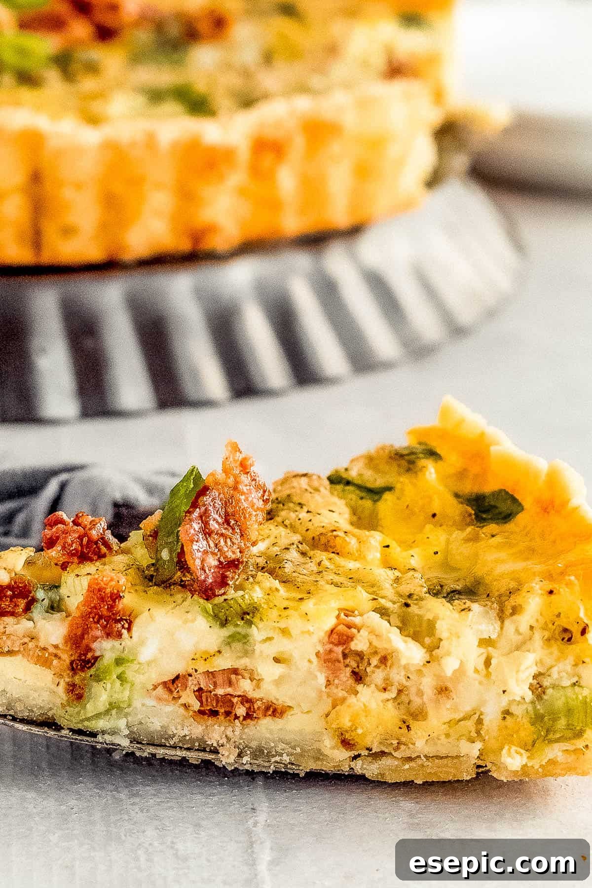 Effortlessly Delicious Bacon Quiche Lorraine 8 A close-up shot of a perfect slice of Bacon Quiche Lorraine being lifted with a metal serving spatula, highlighting its creamy filling and golden crust.