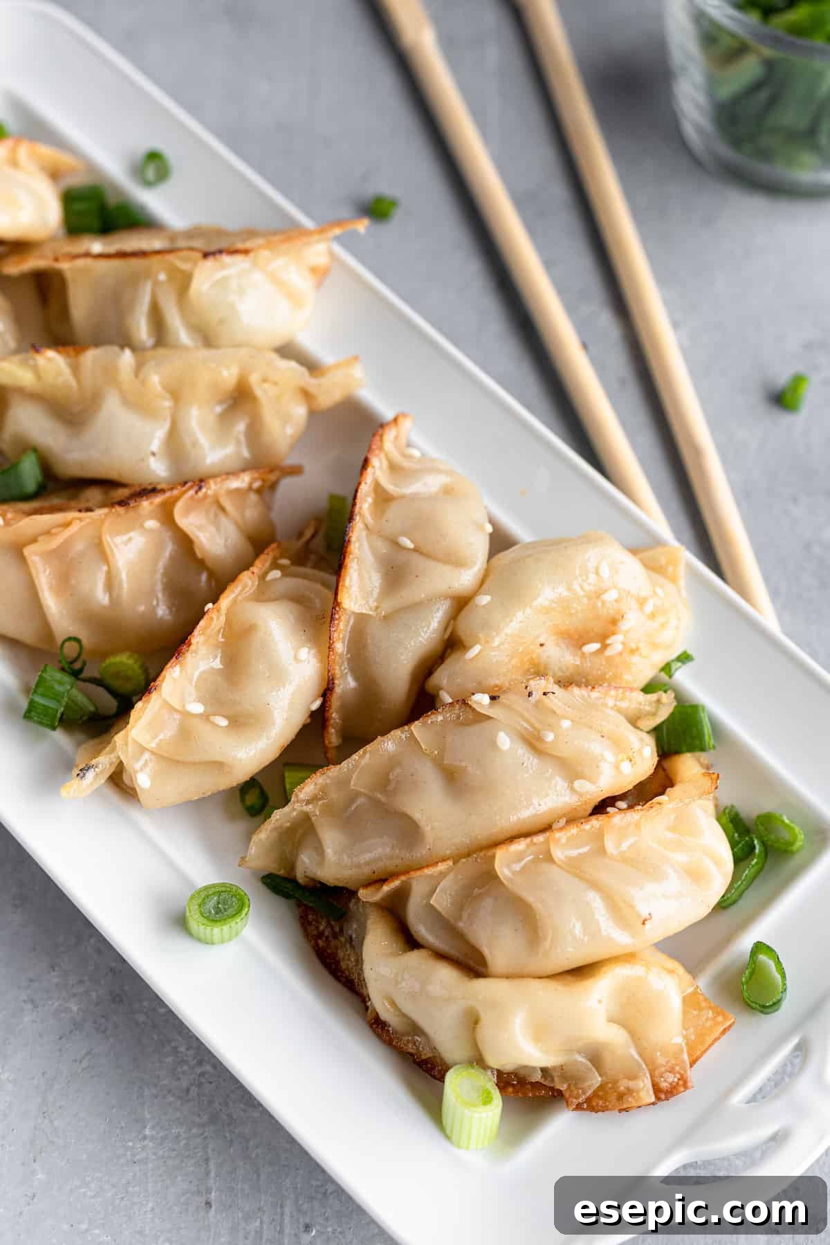 Ten perfectly cooked chicken potstickers arranged on a white serving platter, ready to be enjoyed with chopsticks.