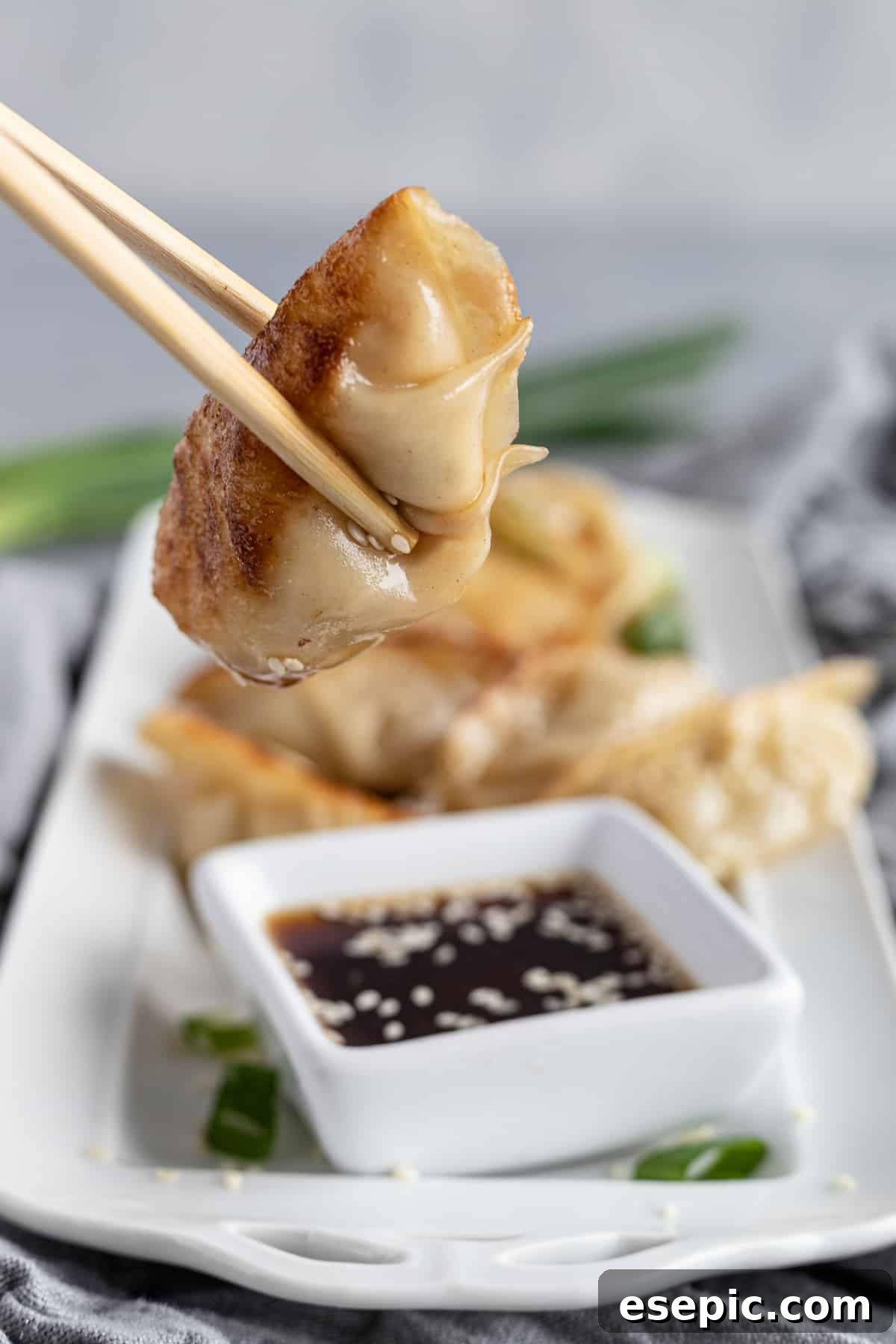 A pair of wooden chopsticks gently squeezing a warm, freshly cooked chicken dumpling.