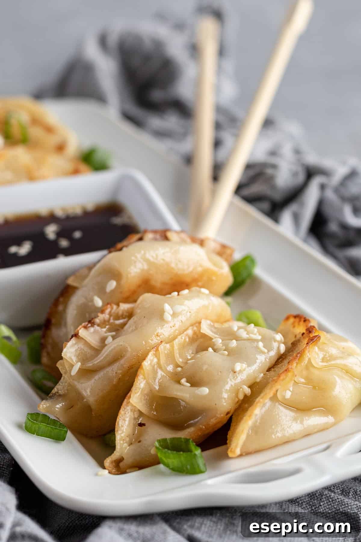 Four golden-brown chicken potstickers on a serving platter, with two chopsticks blurring in the background.