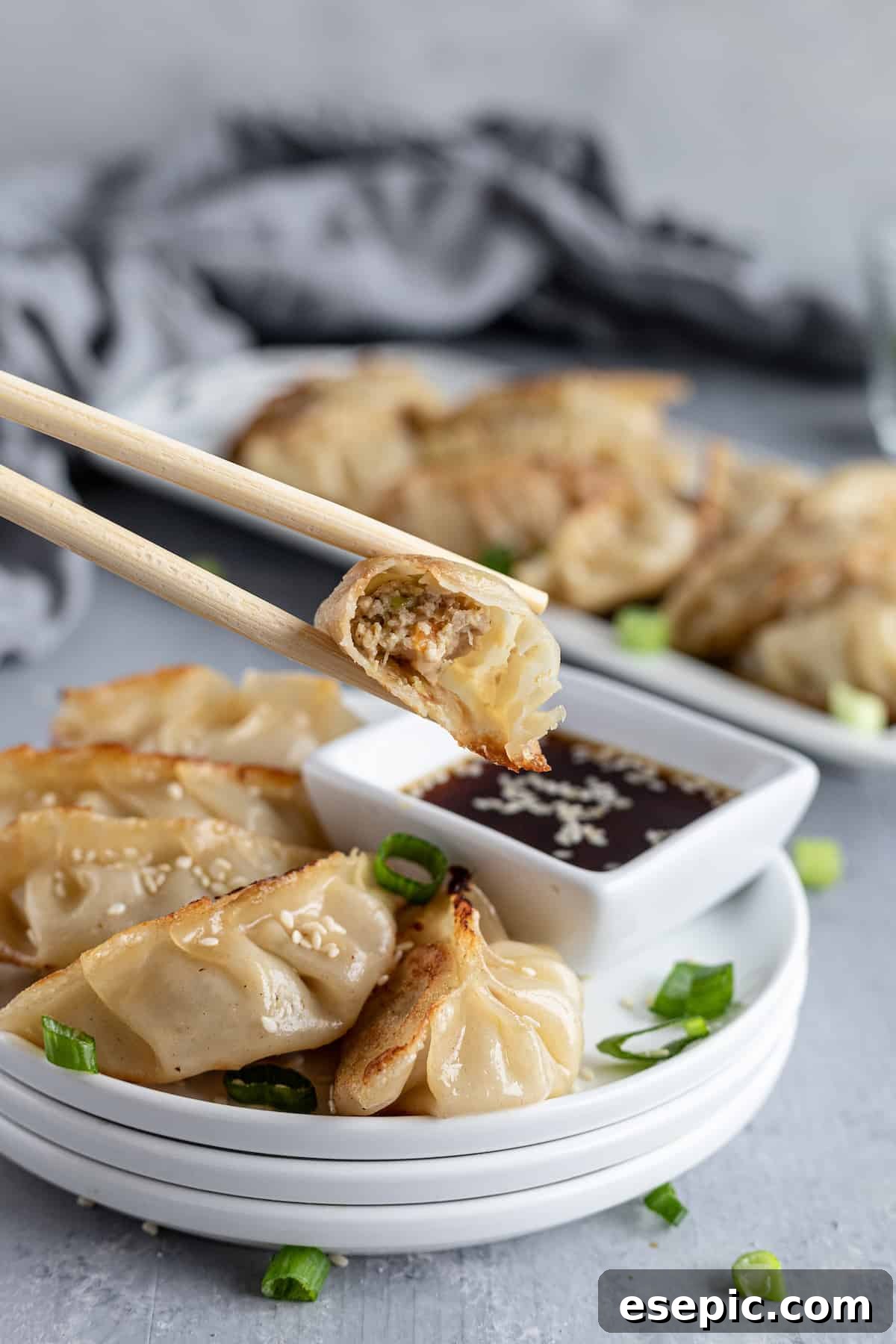 A chicken potsticker held delicately by a pair of wooden chopsticks, showcasing its golden-brown crust.