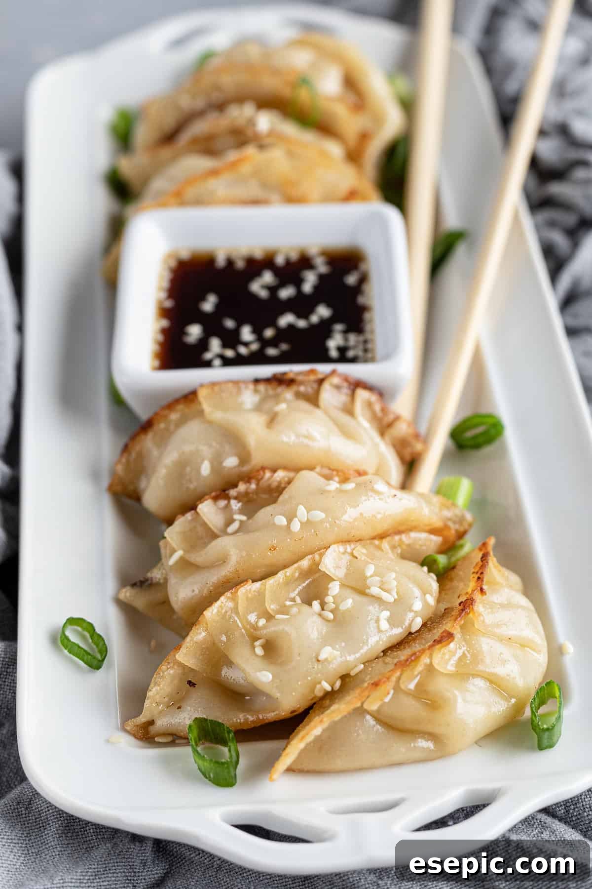 Seven golden-brown chicken dumplings arranged on a serving platter, accompanied by a small bowl of dipping sauce and chopsticks.