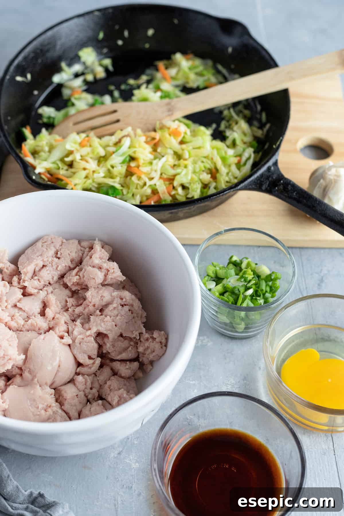 A bowl of ground chicken, a dish of soy sauce, and various fresh filling ingredients laid out on a table, ready for potsticker preparation.