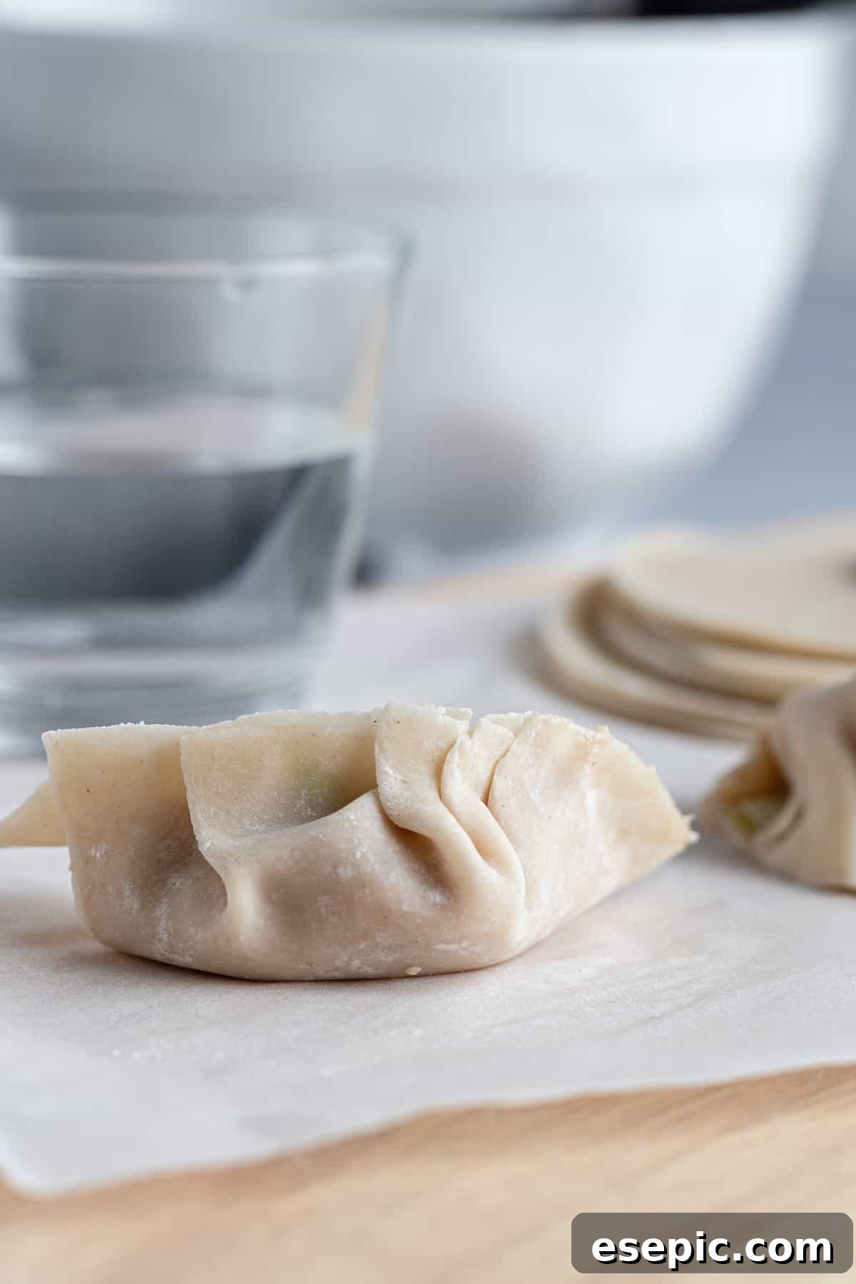 A perfectly formed and sealed chicken dumpling resting beside a small dish of water.