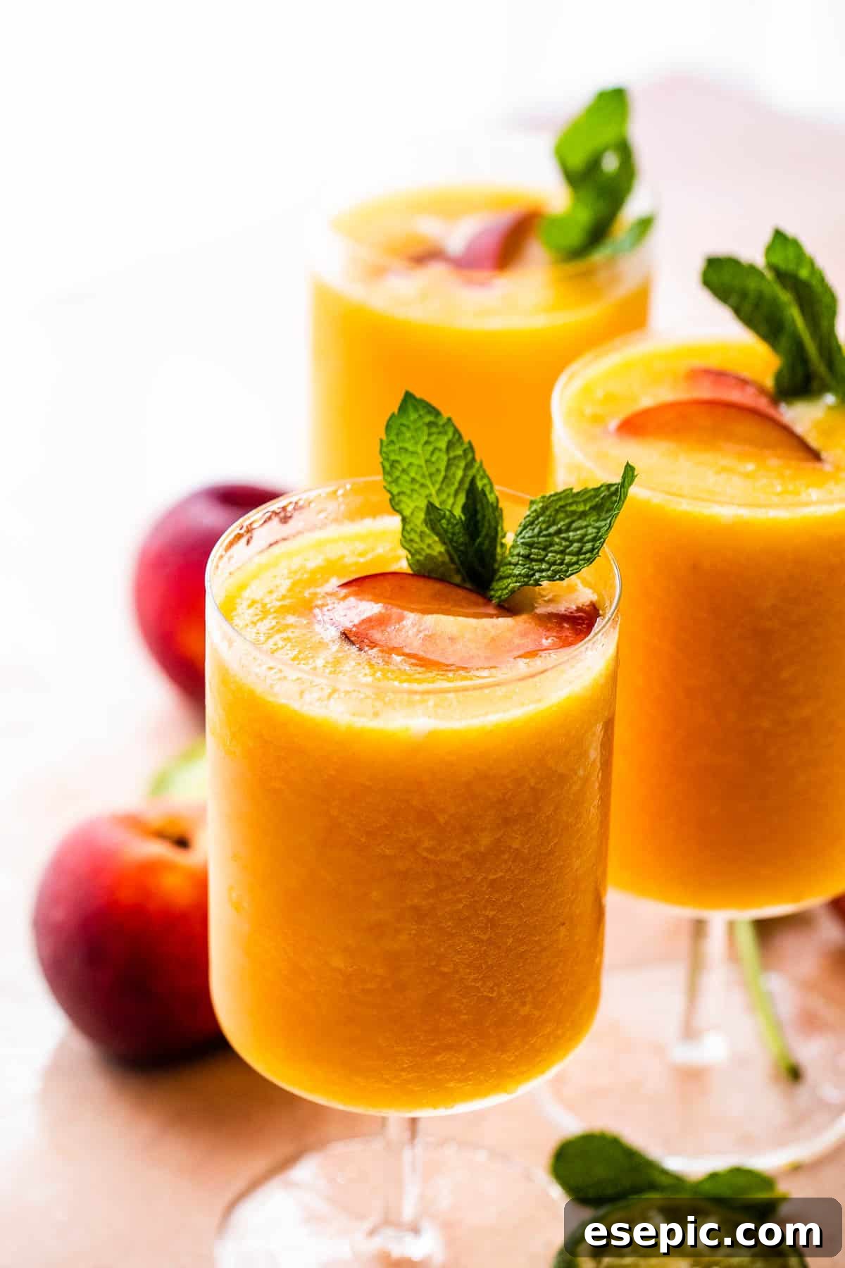 Sweet and refreshing Peach Daiquiri made with fresh peaches, lime juice, and white rum – a perfect summer cocktail! three glasses filled with peach daiquiris, garnished with mint and peach slices, showcasing a perfect summer drink