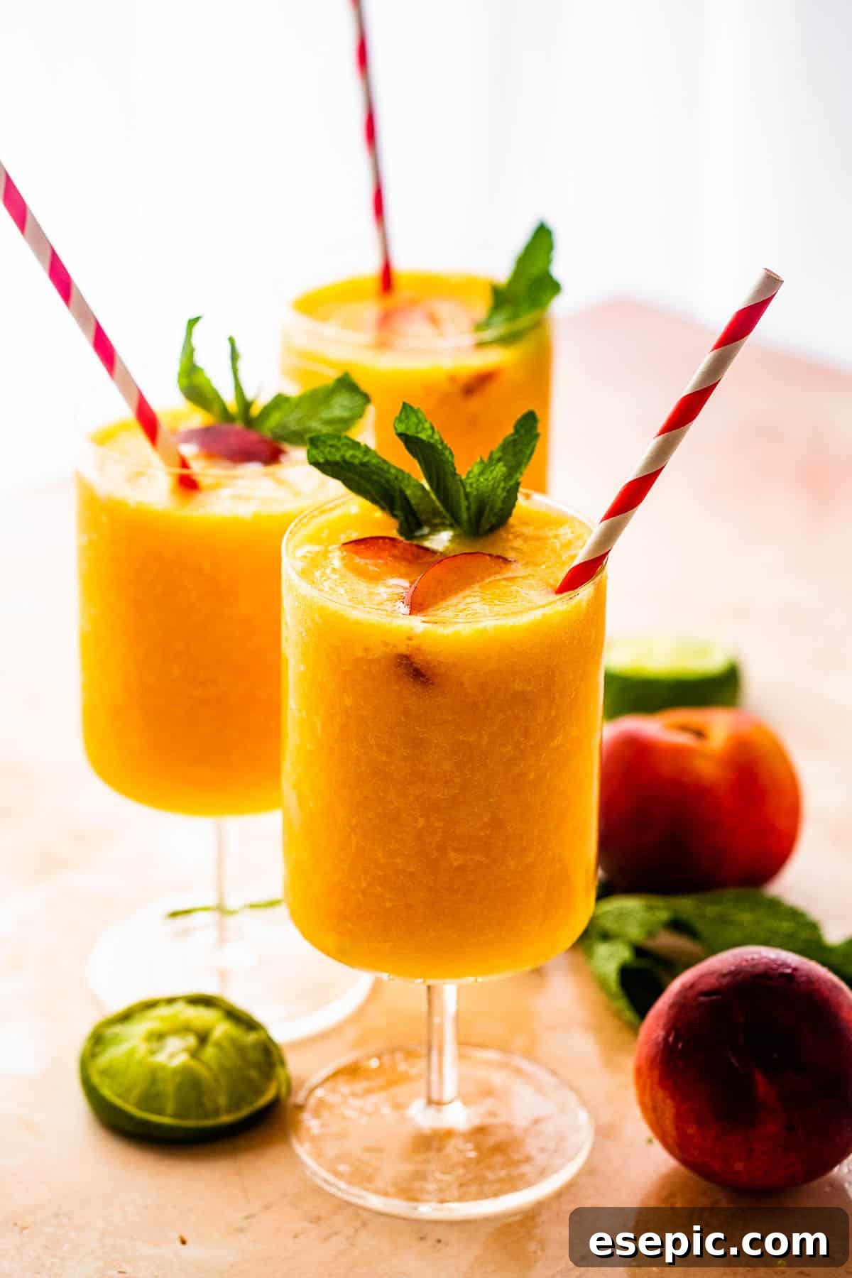 Sweet and refreshing Peach Daiquiri made with fresh peaches, lime juice, and white rum. three glasses filled with peach daiquiris and garnished with mint, peach slices, and straws, showcasing a refreshing summer drink
