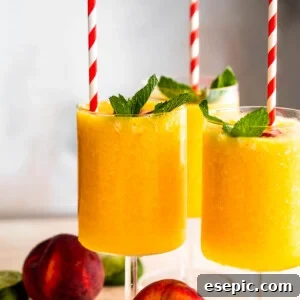 three glasses filled with peach daiquiris and garnished with mint, peach slices, and straws