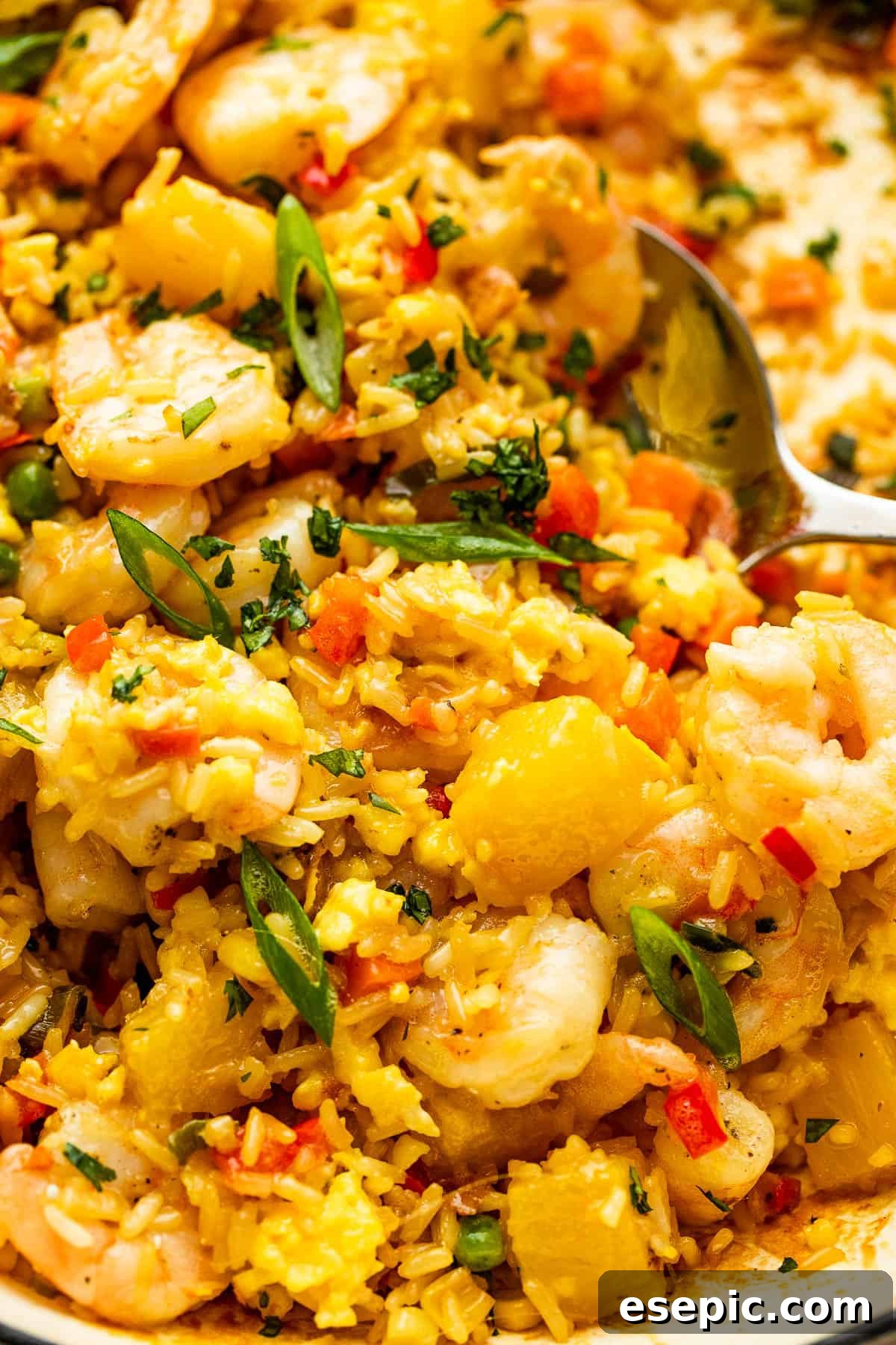 Tropical Pineapple Shrimp Fried Rice 3 Scooping a generous portion of Shrimp Fried Rice with a large stainless spoon from a skillet.
