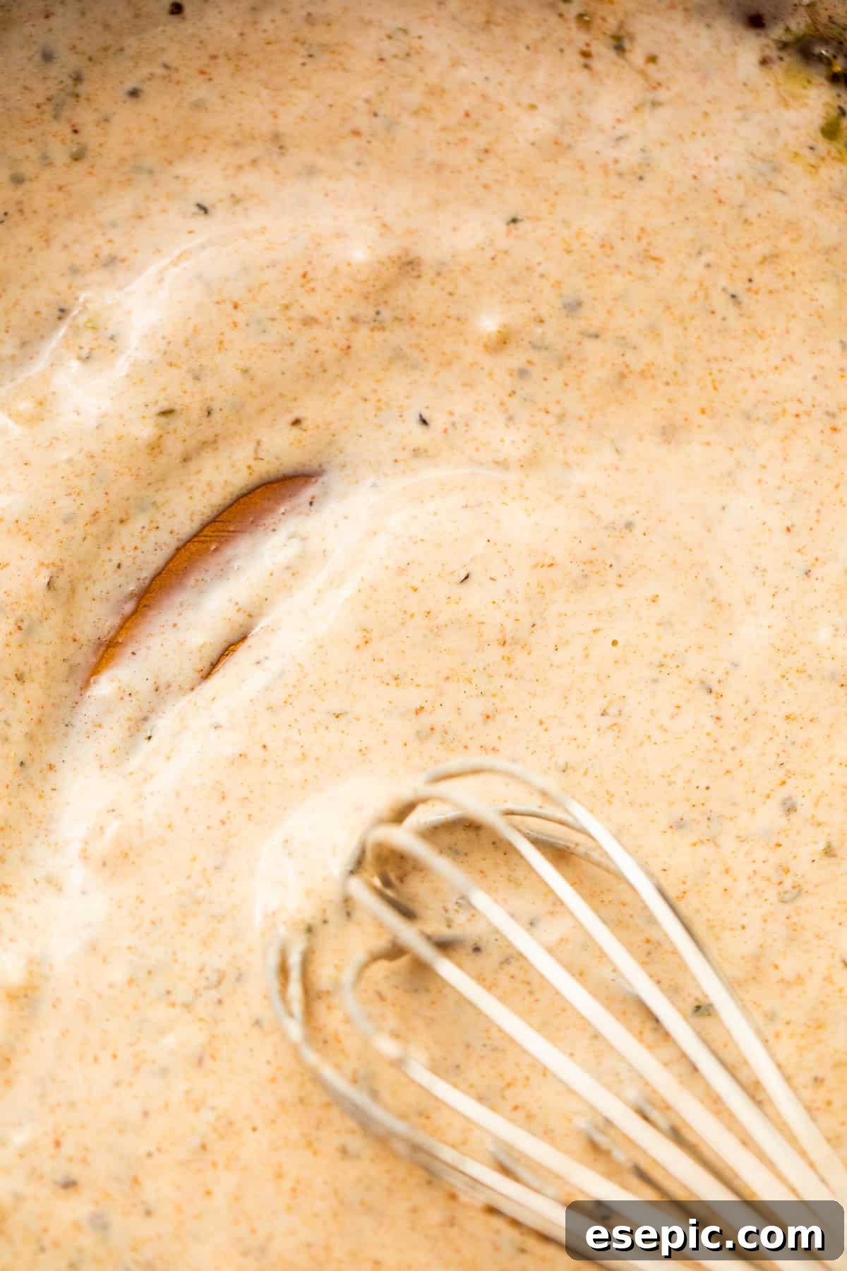 Hands whisking a creamy dressing in a glass bowl, showcasing the smooth texture before it is added to the pasta salad.